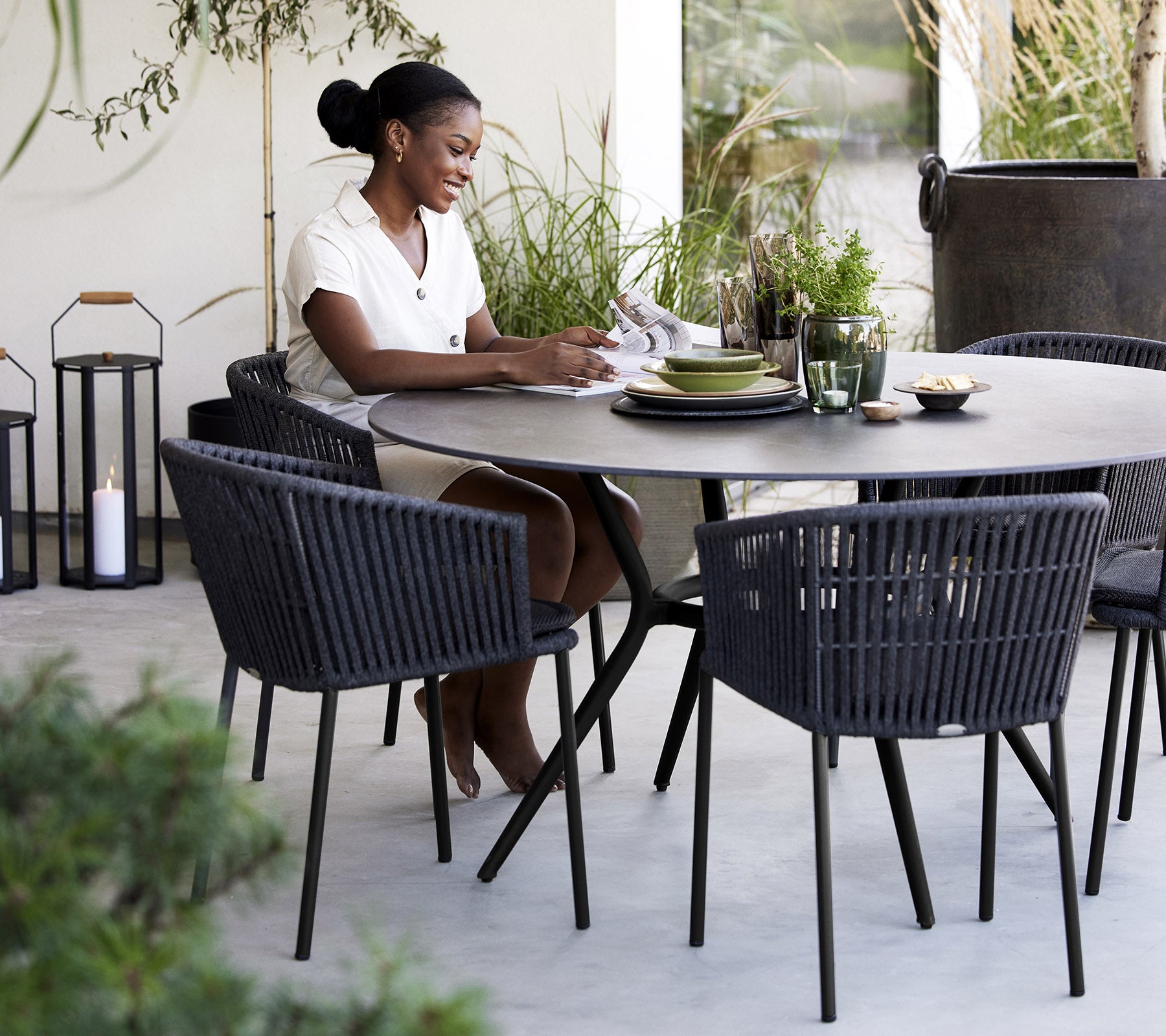 Une femme assise à une table ronde, savourant un repas, entourée de chaises élégantes et de plantes.
