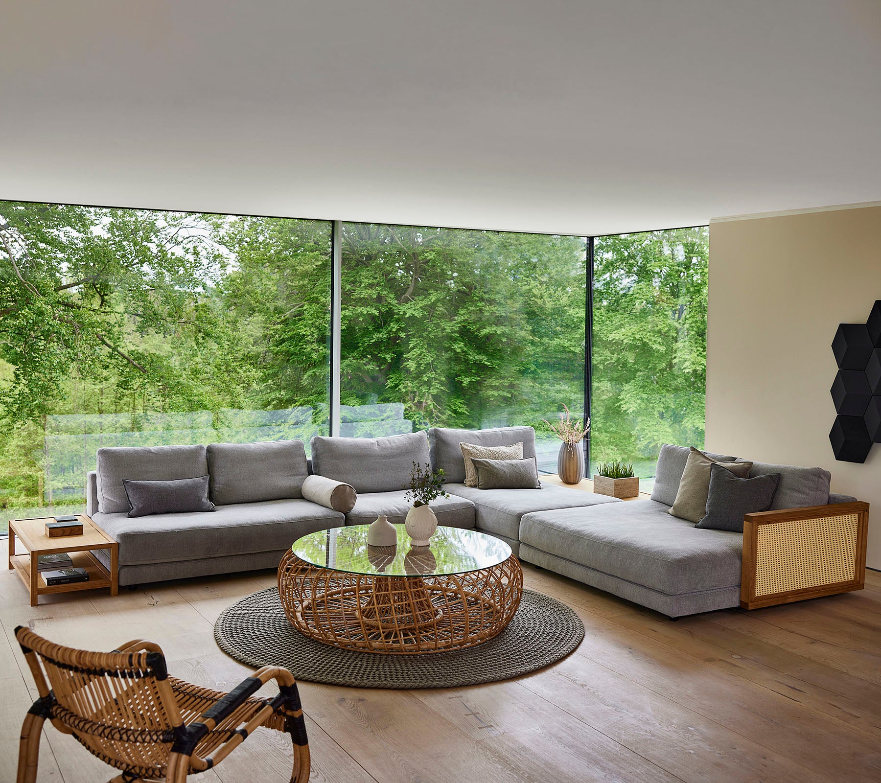Un espace de détente moderne avec un canapé sectionnel gris, une table basse ronde et une chaise tissée, entouré de verdure.