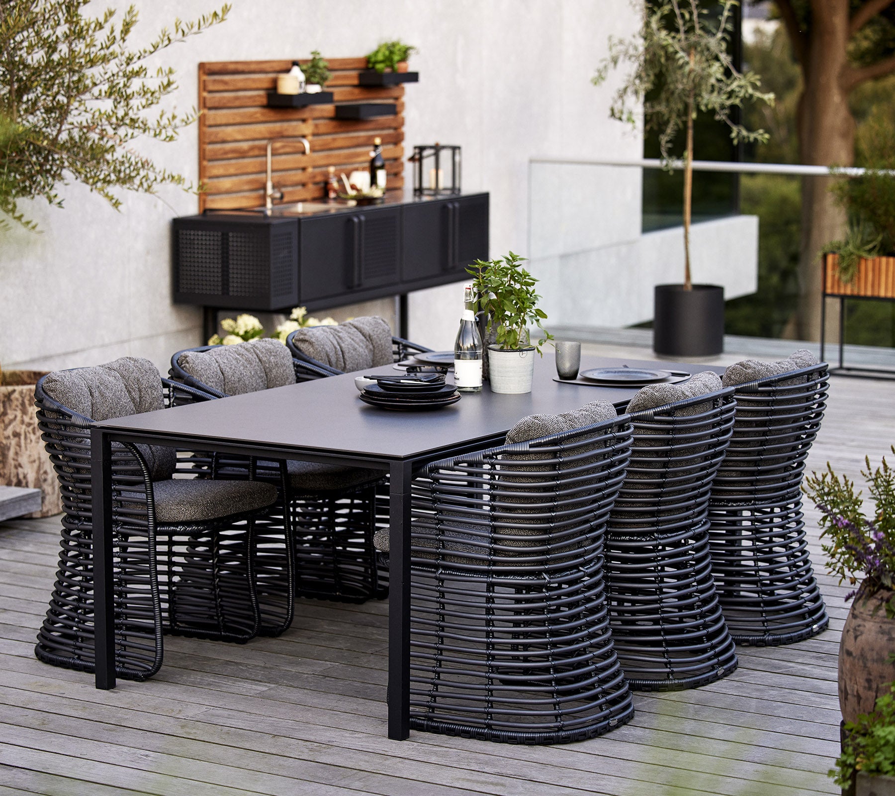 Un ensemble de salle à manger moderne comprenant une table rectangulaire et six chaises en osier élégantes, complété par des éléments décoratifs en arrière-plan.