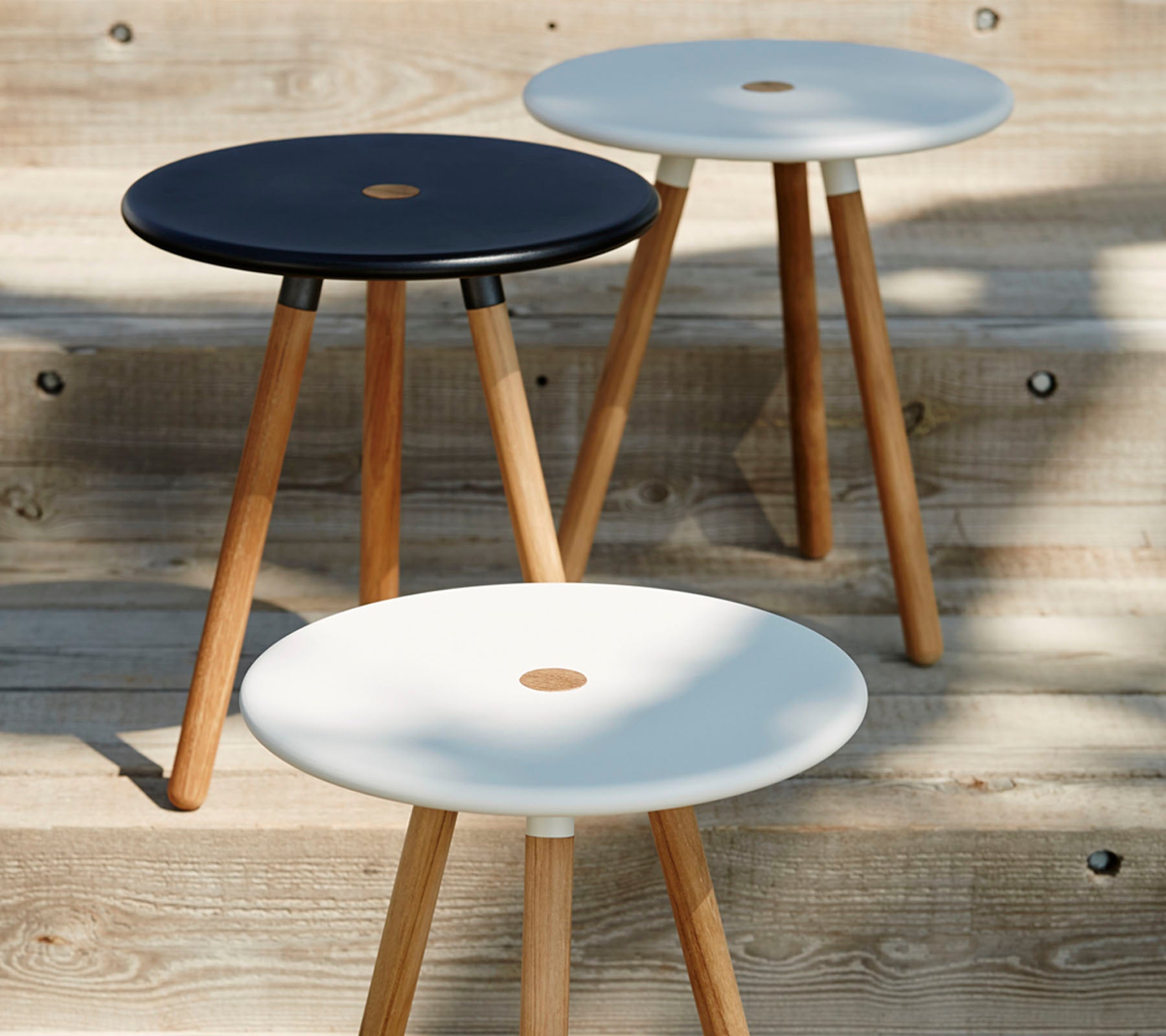 Trois tabourets minimalistes avec des assises rondes en noir et blanc, tous soutenus par des pieds en bois, mettant en avant un design moderne et élégant.