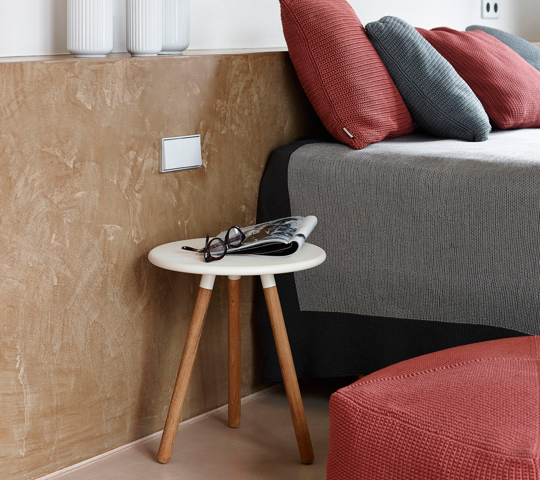 Une scène de chambre confortable avec une table basse, des lunettes et un magazine à côté d'un lit bien fait avec des coussins texturés.