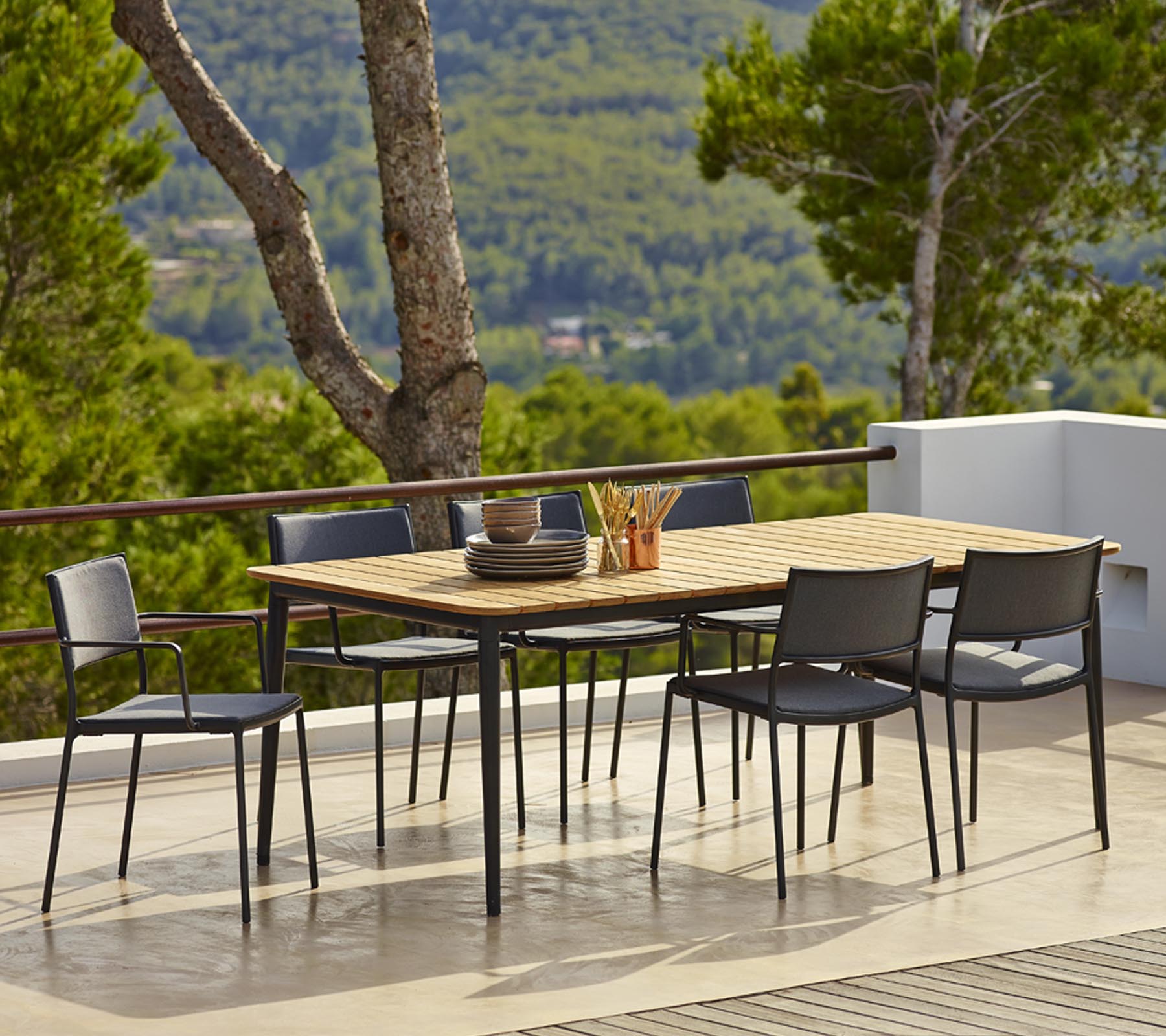 Ensemble de table de salle à manger d'extérieur avec un plateau en bois rectangulaire et des chaises noires, entouré de verdure et de vues pittoresques.