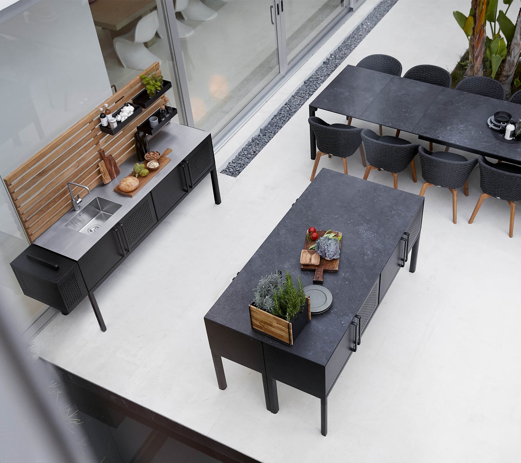 Installation moderne de cuisine extérieure avec un comptoir élégant, une grande table à manger et un agencement de sièges élégant avec des plantes et des éléments décoratifs.