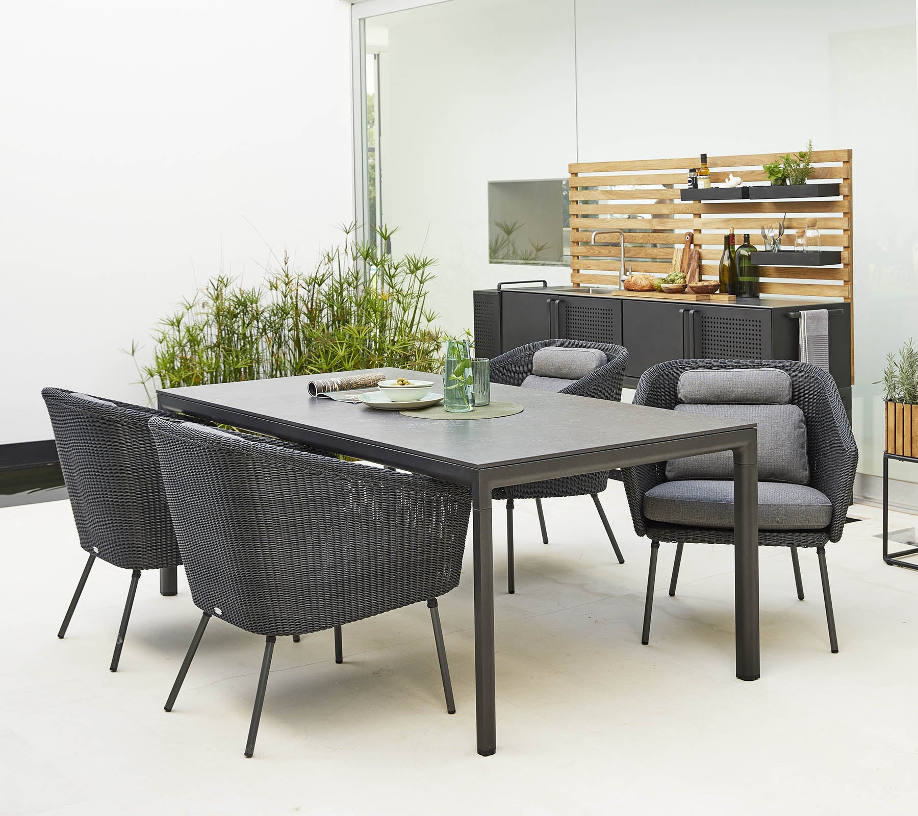 Ensemble de salle à manger d'extérieur élégant comprenant une table épurée et des chaises modernes et confortables entourées de verdure décorative.