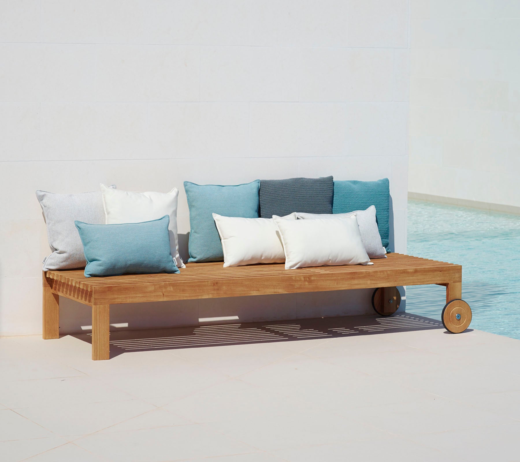 Canapé en bois avec un design simple, équipé de coussins dans des teintes de bleu et de blanc, placé à côté d'une piscine.