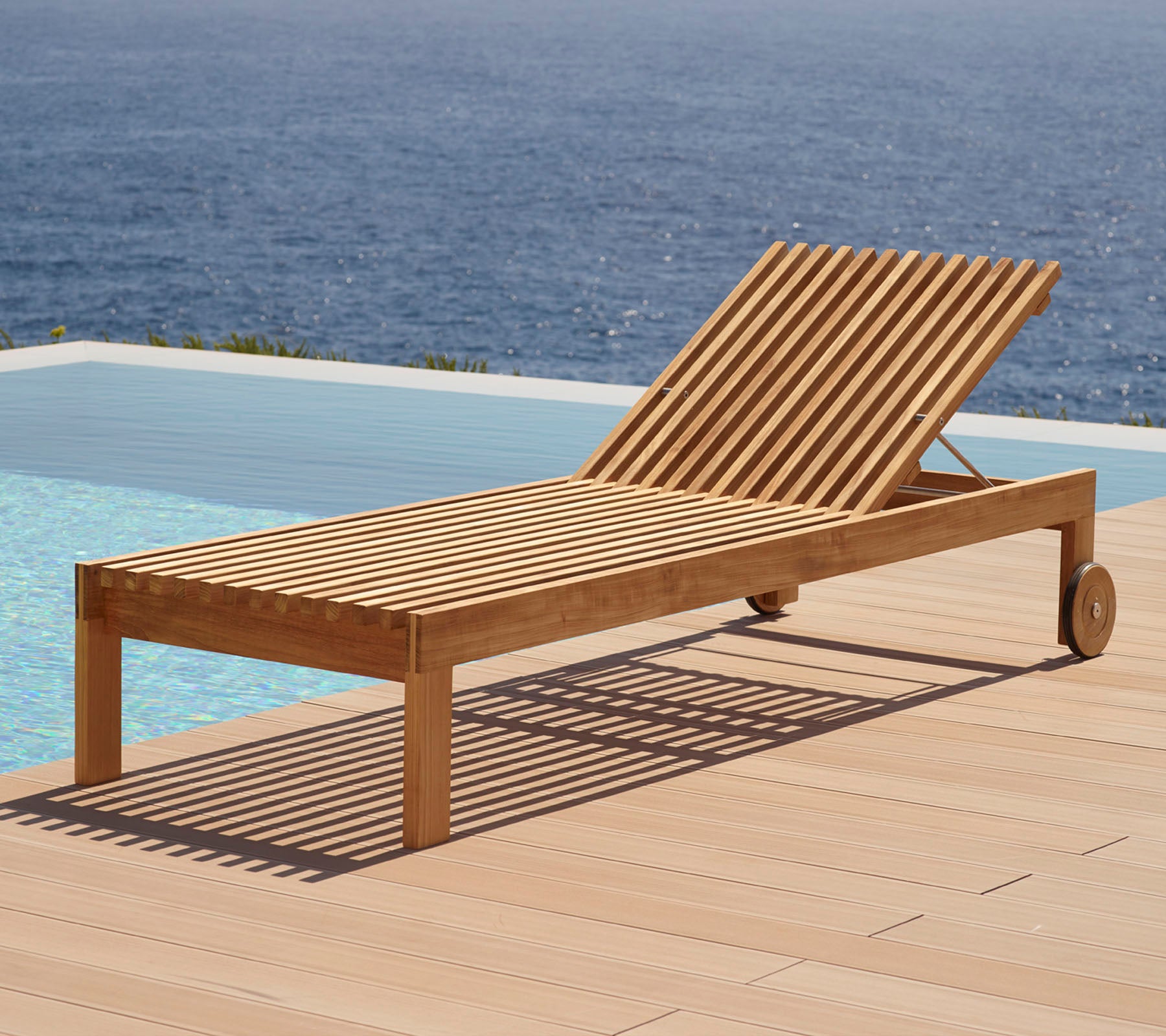 Chaise longue en bois avec un design à lattes, équipée de roues et positionnée à côté d'une piscine avec vue sur l'eau en arrière-plan.