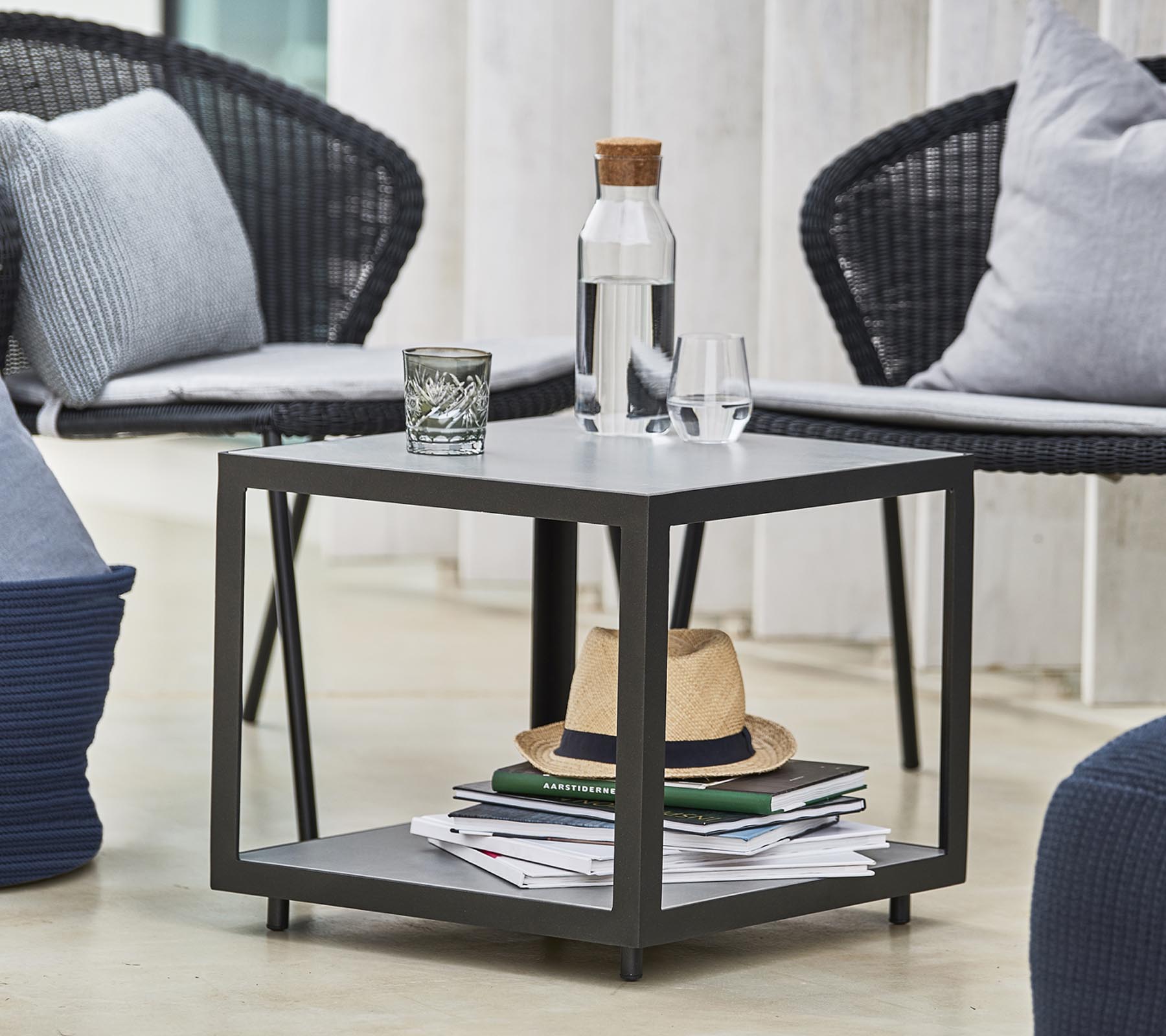 Une table moderne avec une bouteille d'eau, un verre et des objets décoratifs, entourée de chaises élégantes et de coussins.