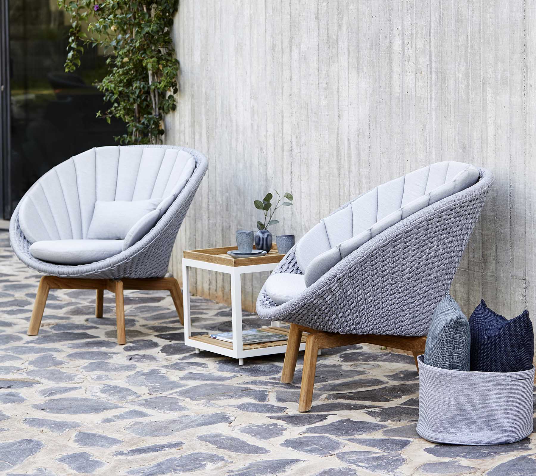 Deux fauteuils modernes gris avec un cadre en bois sont placés à côté d'une table d'appoint blanche, ornée d'une petite plante et de coussins décoratifs.