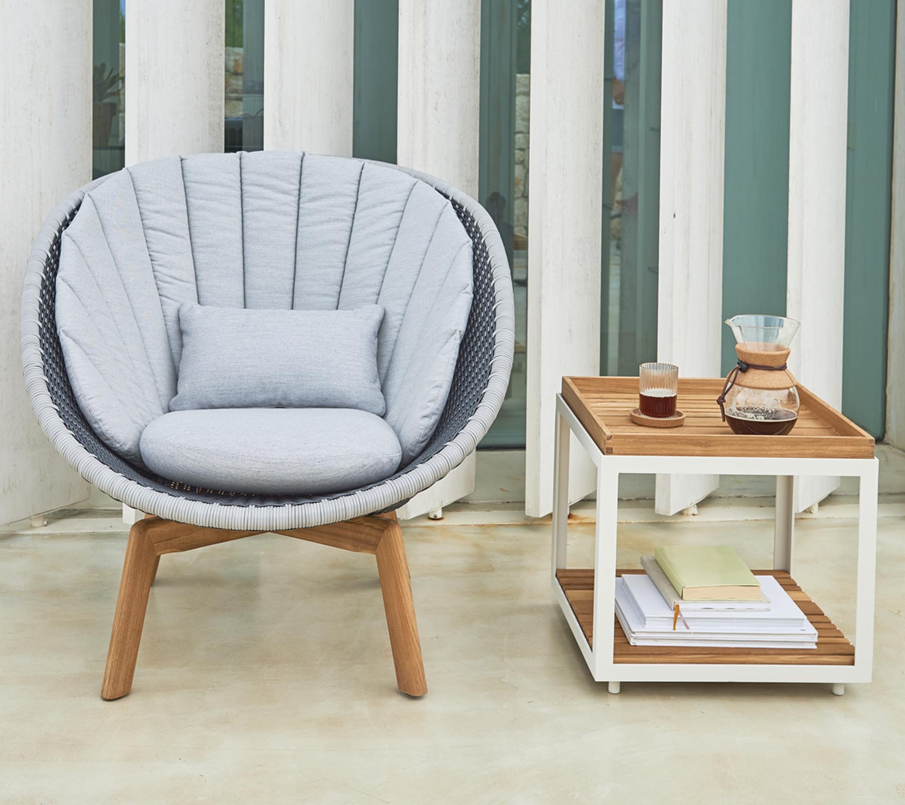 Chaise ronde et confortable avec des coussins moelleux à côté d'une table d'appoint soignée contenant des boissons et des livres.