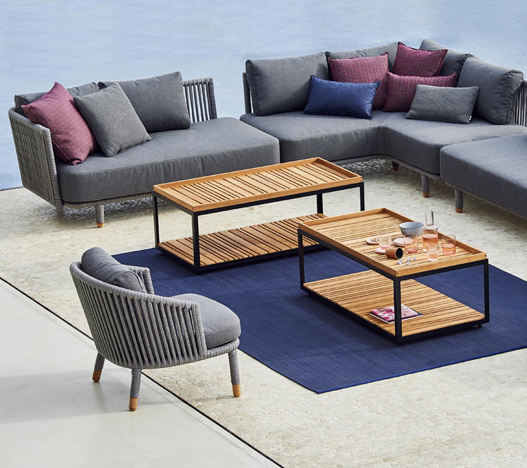 Aménagement moderne avec un canapé d'angle gris, une chaise ronde élégante et des tables basses en bois avec un tapis bleu en dessous.