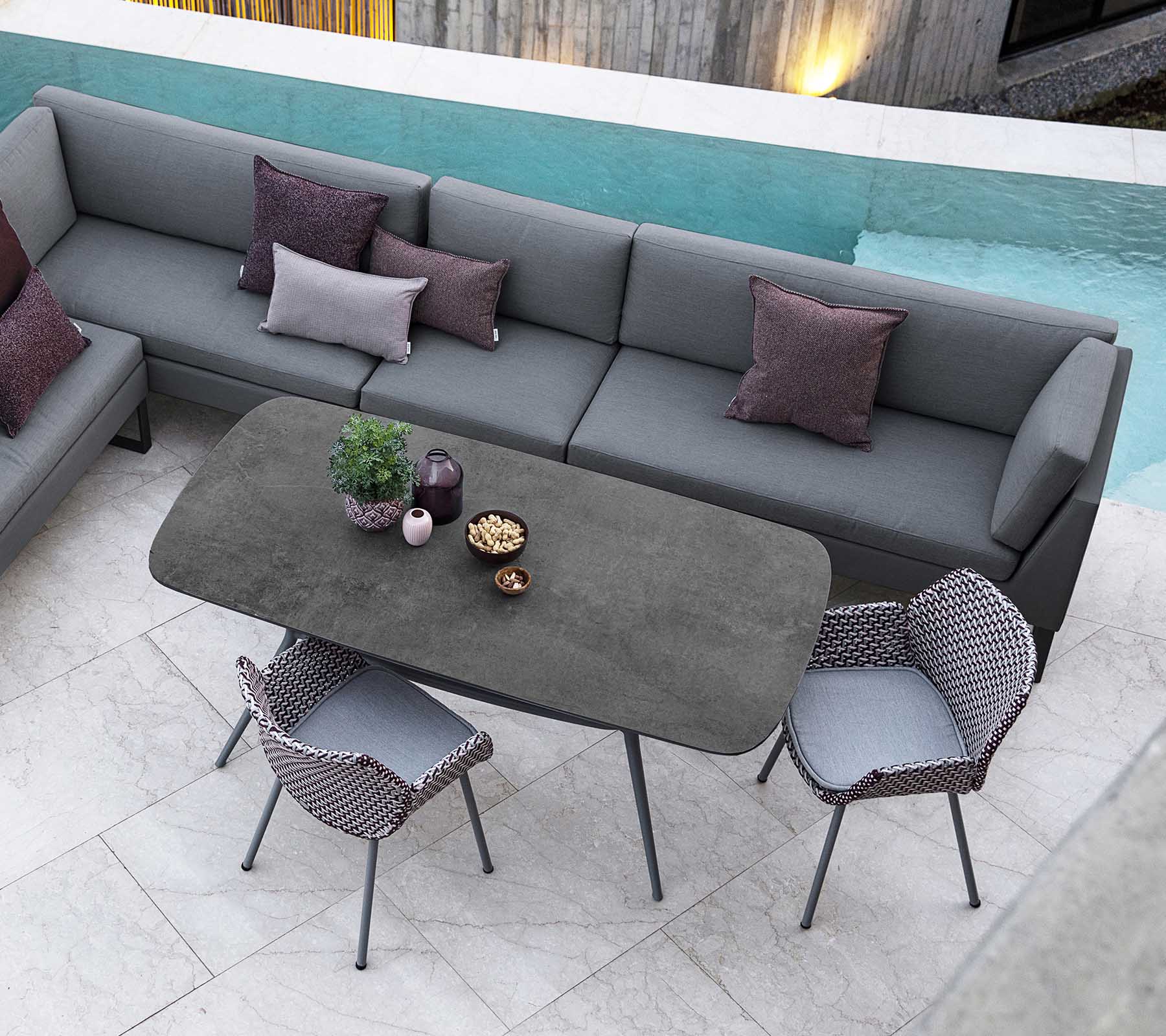 Espace extérieur moderne avec un canapé modulable et des coussins, une table rectangulaire élégante et des chaises élégantes, complété par une vue sur la piscine.