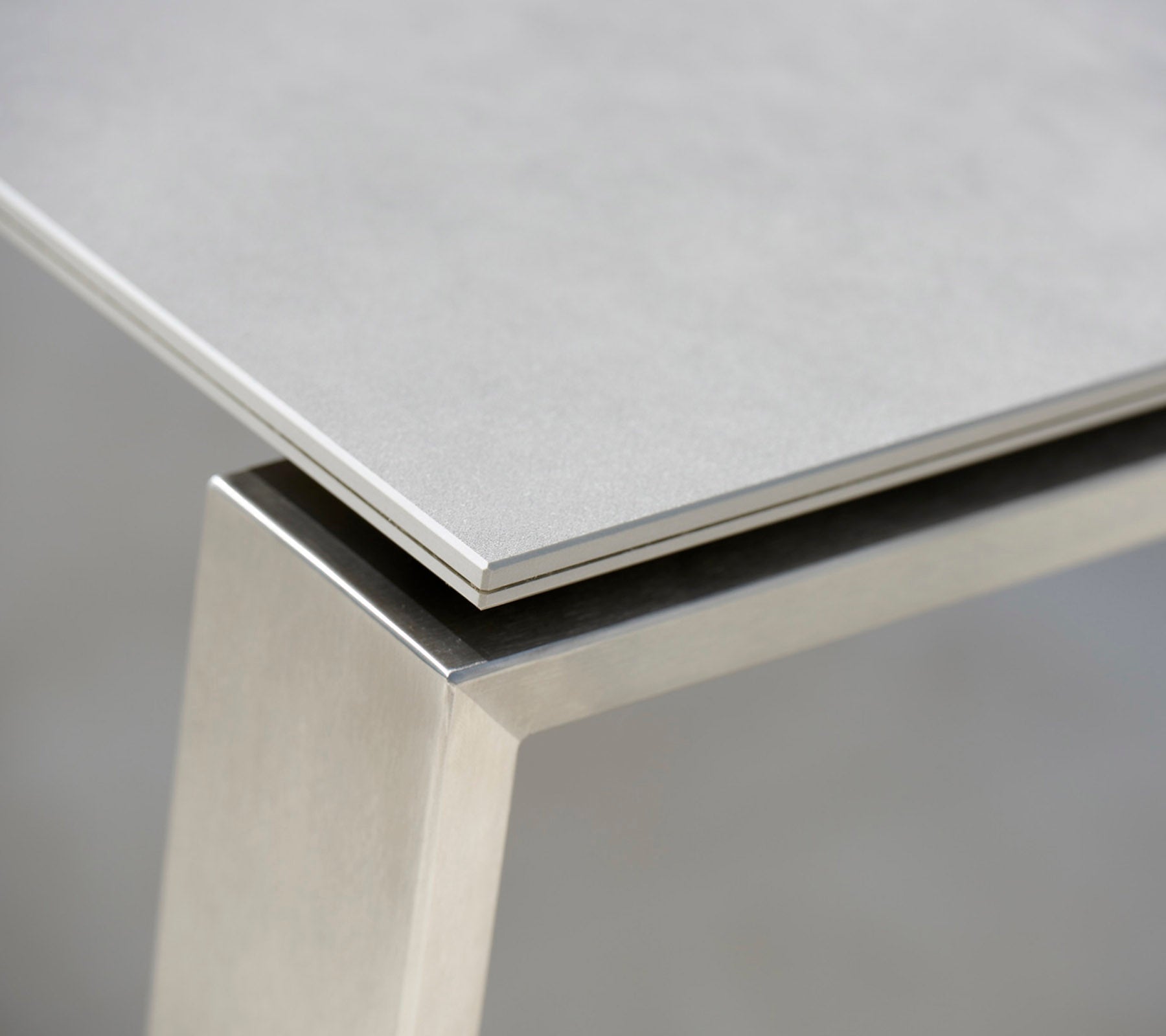 Gros plan sur une table moderne avec un dessus gris élégant et une base en acier inoxydable, mettant en valeur les matériaux contrastants et les lignes épurées.