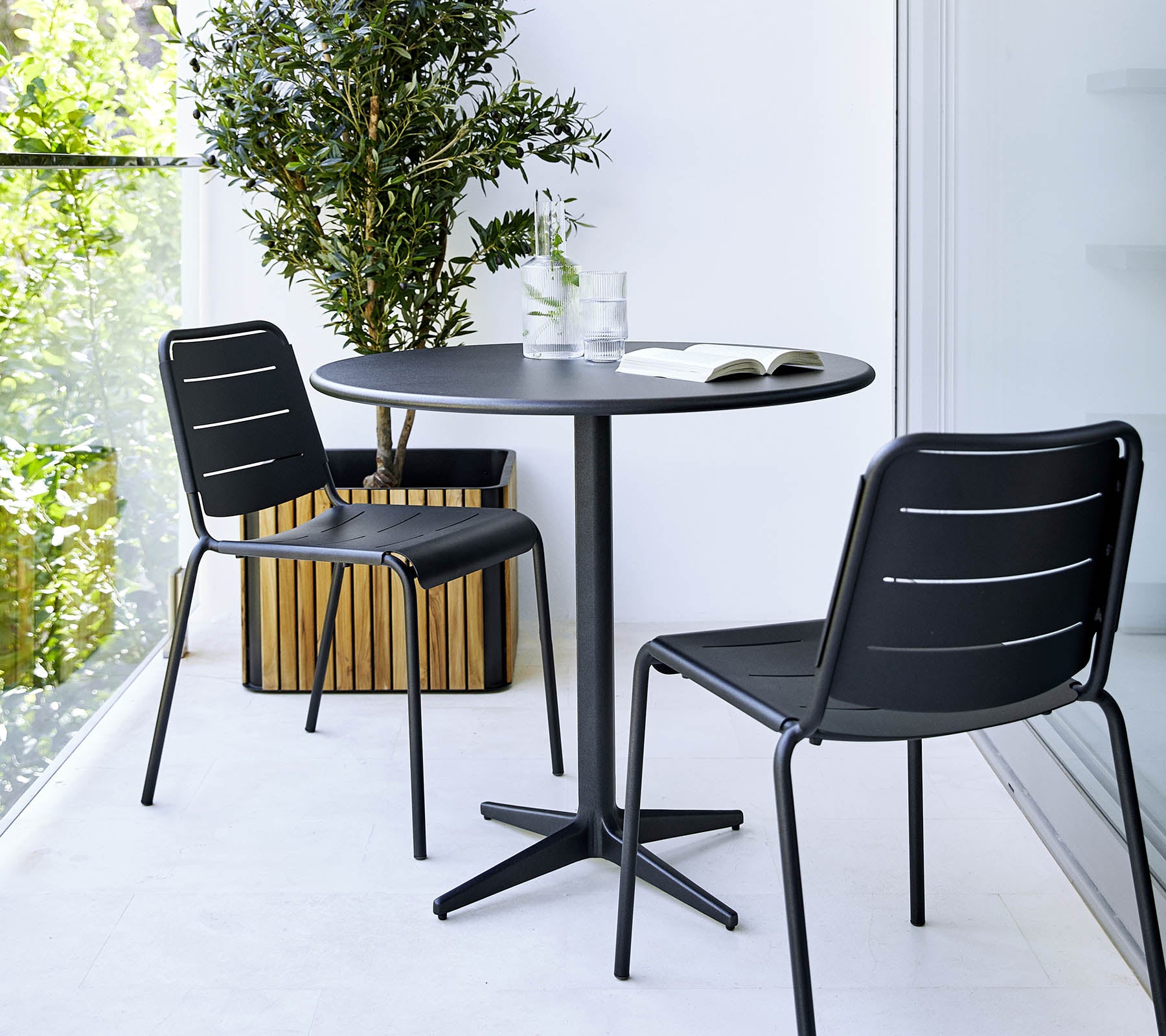 Petite table ronde avec deux chaises noires et une plante en pot à proximité, créant une ambiance minimaliste et élégante.