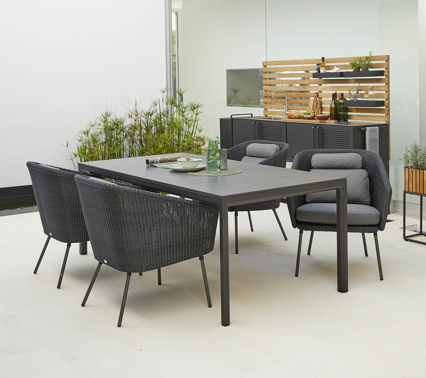 Ensemble de salle à manger moderne pour l'extérieur avec une table élégante et quatre chaises stylées avec des coussins confortables, entouré de verdure.