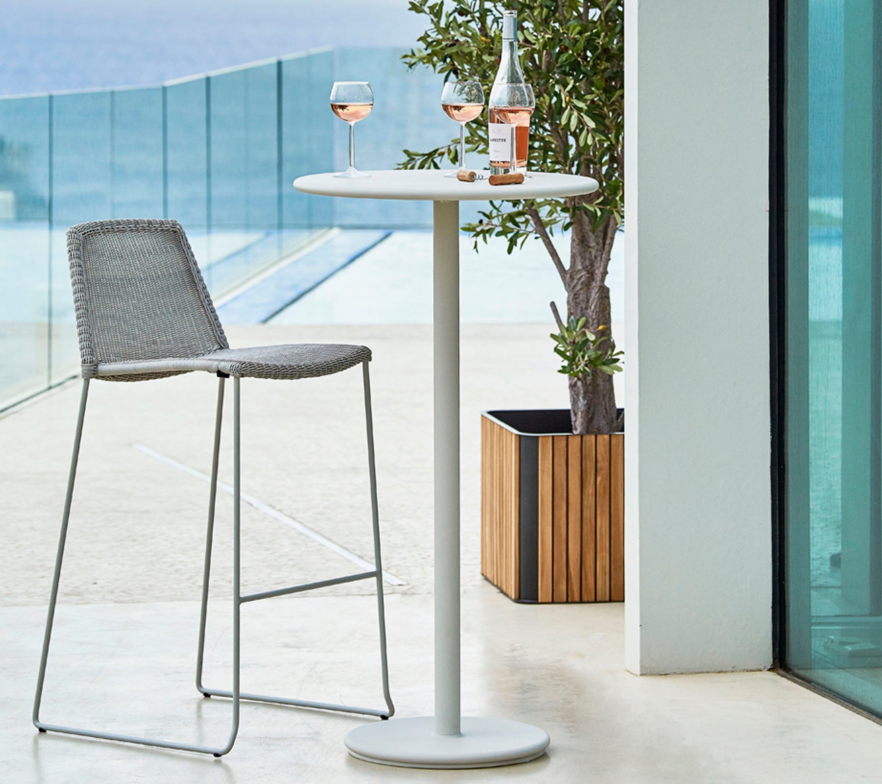 Cadre extérieur élégant avec une haute table, un tabouret de bar gris et deux verres de rosé accompagnés d'une bouteille sur la table.