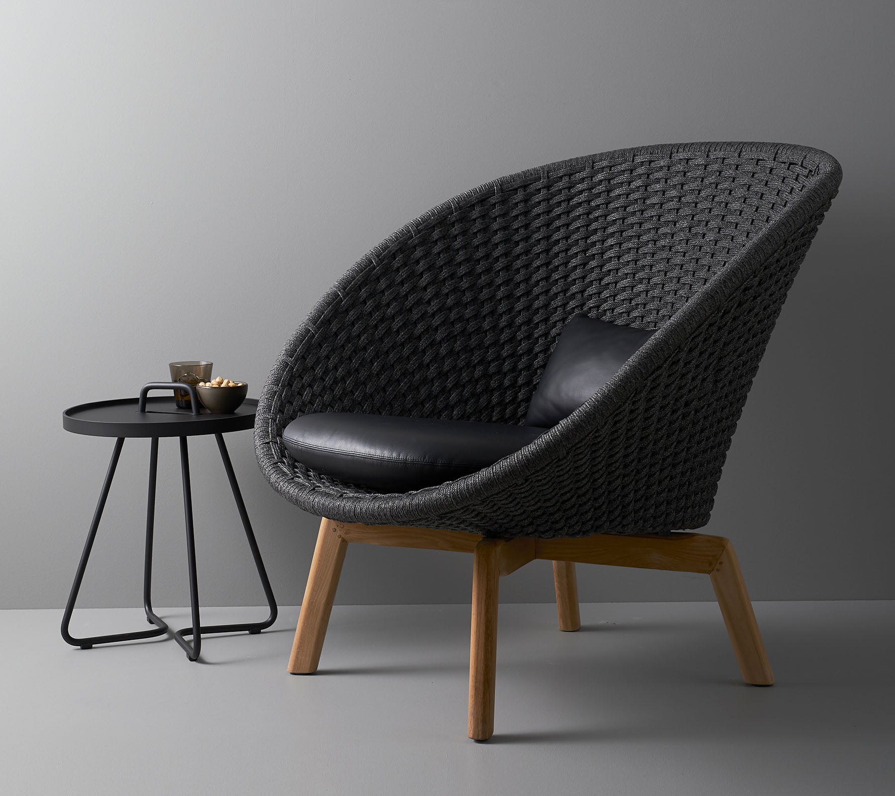 Chaise tressée élégante avec un coussin noir et une table d'appoint ronde moderne, idéale pour des espaces de vie contemporains.