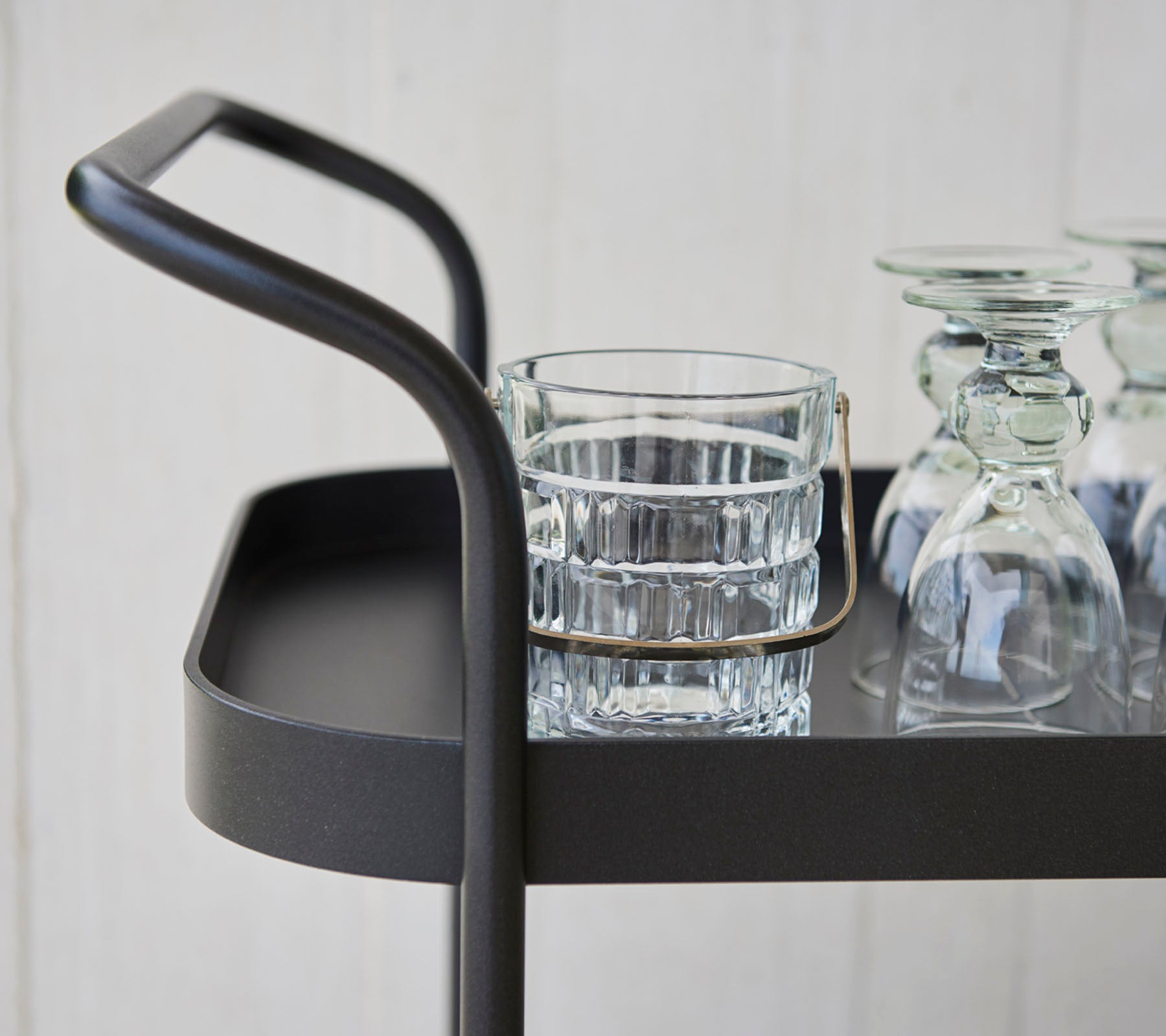 Chariot de service élégant avec une poignée fine, comprenant un verre et plusieurs pièces en verre transparent sur une surface plate.