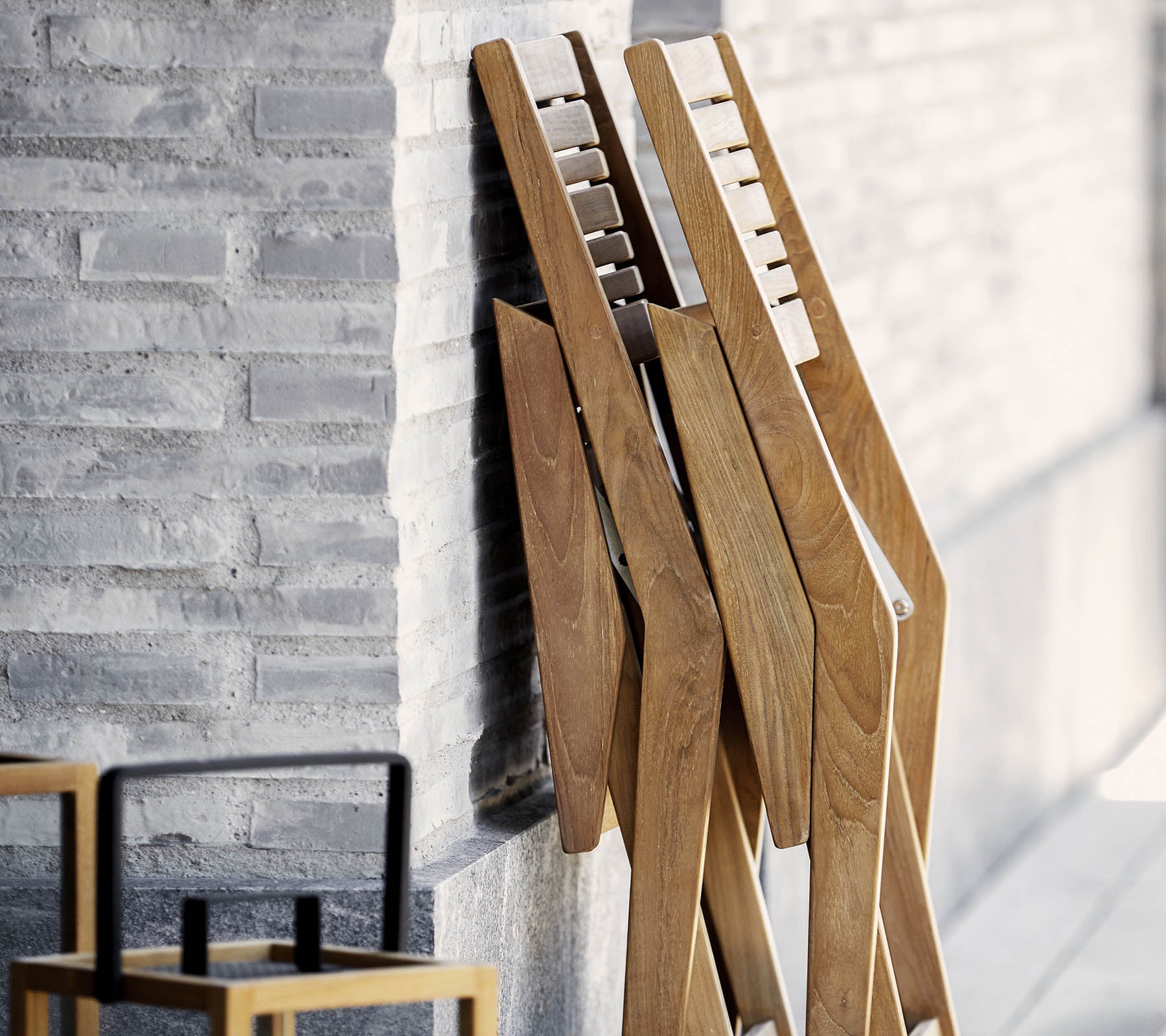 Trois supports en bois au design épuré, adossés à un mur texturé, accompagnés d'une simple et élégante chaise au premier plan.