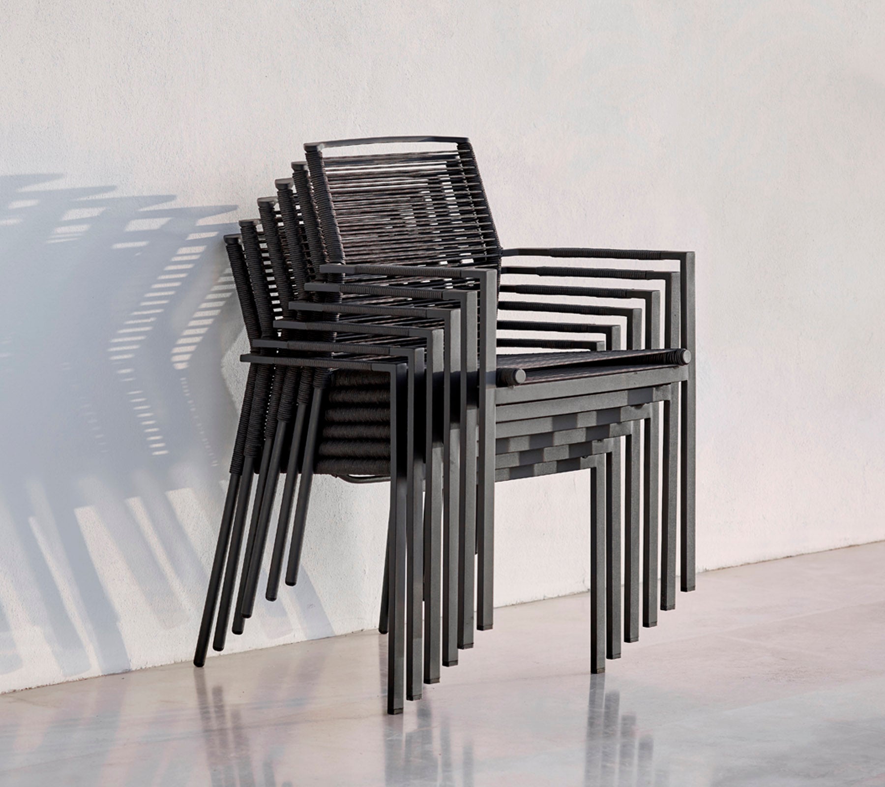 Une pile de chaises noires modernes au design épuré, projetant des ombres sur un fond clair.