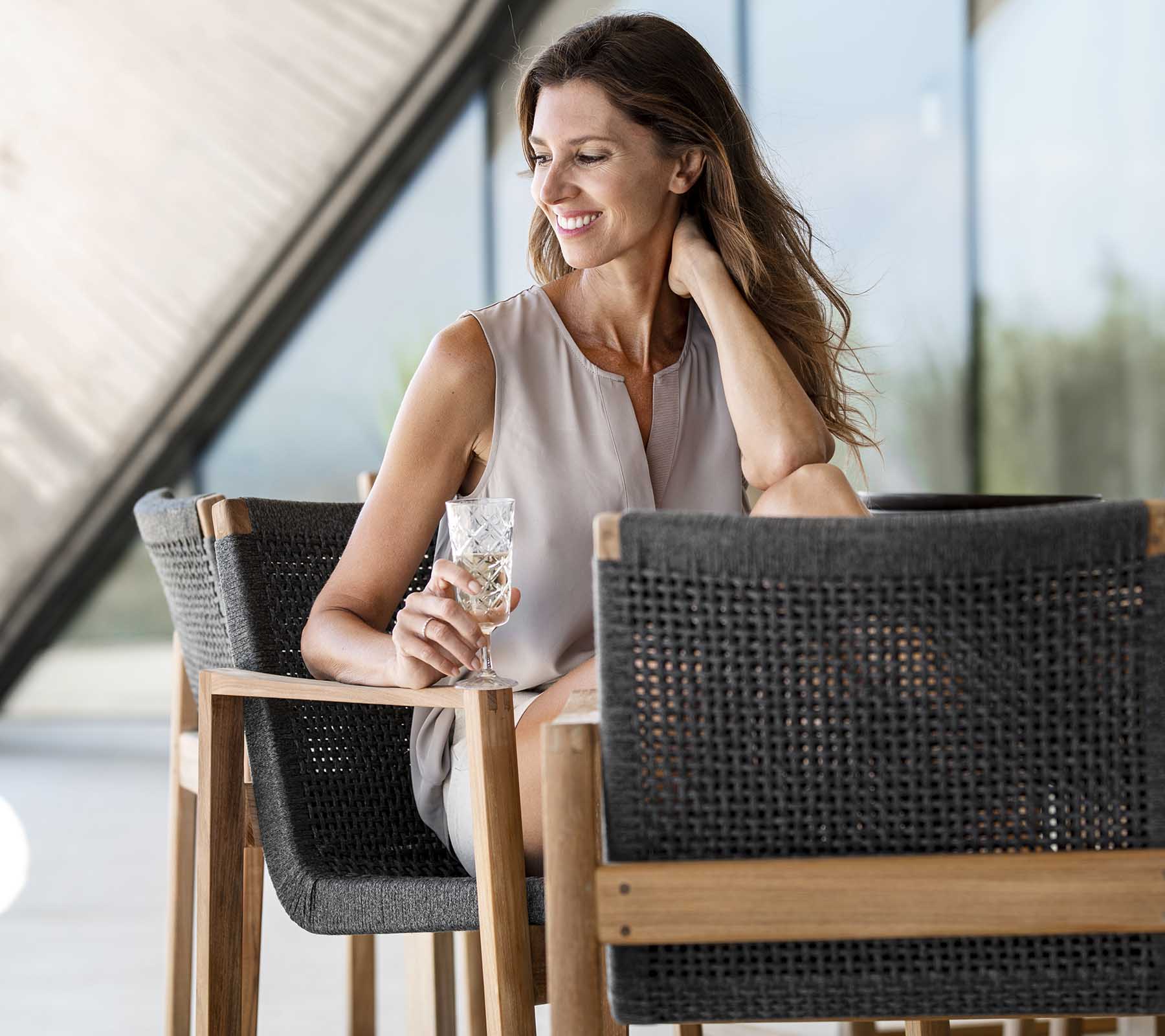 Femme souriante tenant une boisson assise sur une chaise élégante, dégageant une ambiance détendue et élégante. Atmosphère lumineuse et aérée.