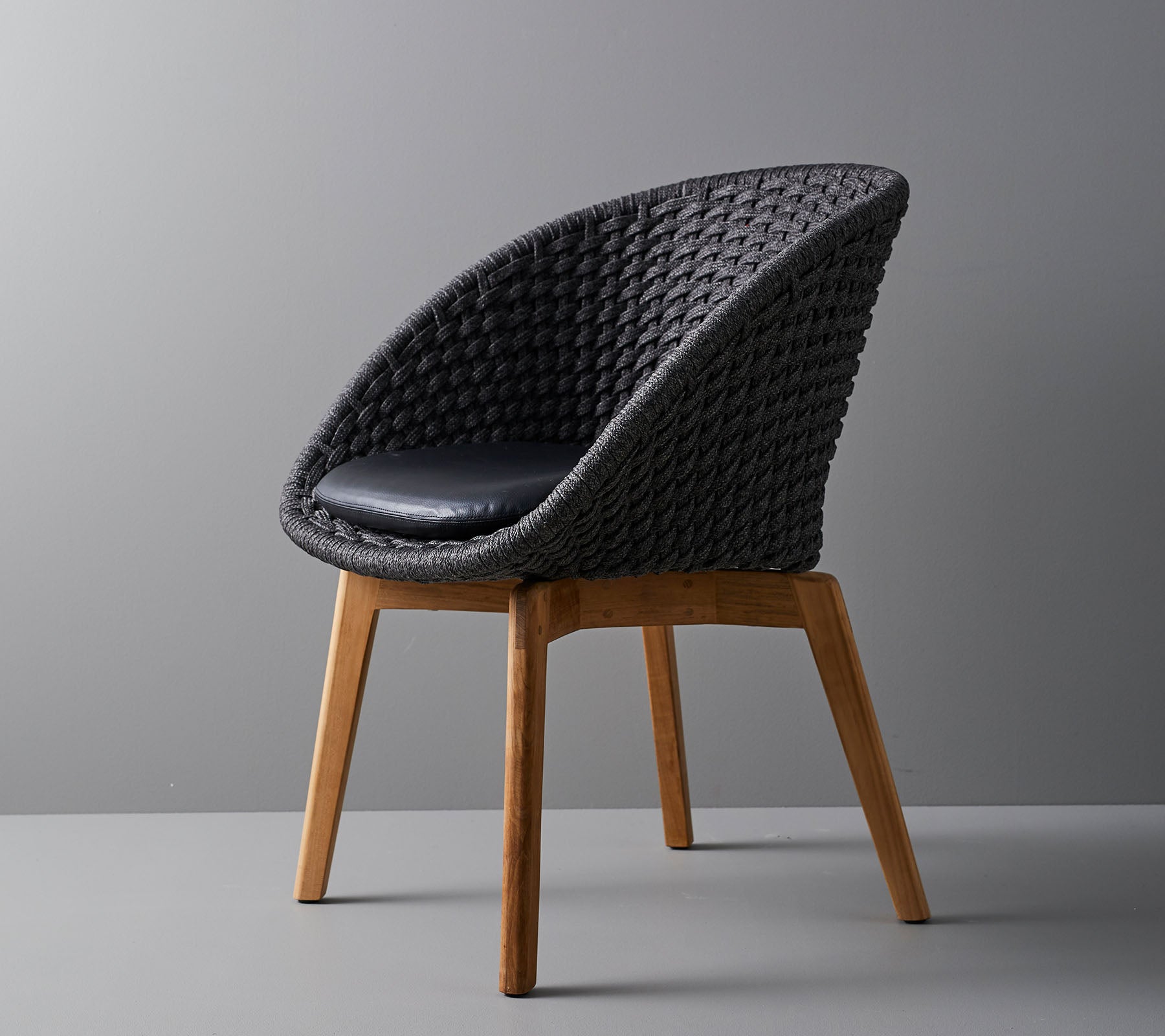 Chaise tissée élégante avec un coussin confortable, dotée de pieds en bois lisses et effilés, et d'un design moderne adapté à divers environnements.