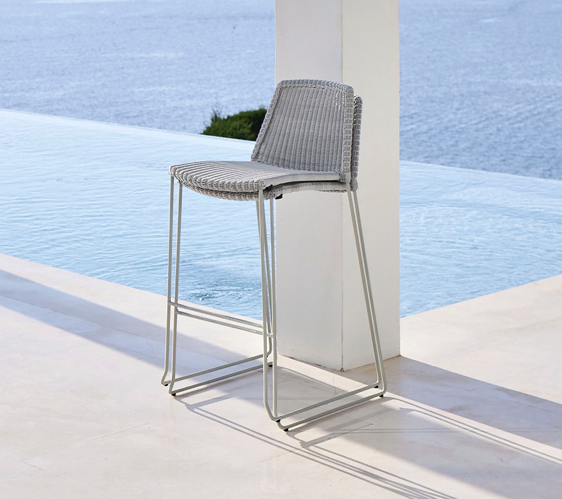 Tabouret de bar élégant avec un siège tissé et des pieds métalliques sleek, positionné près d'une caractéristique d'eau tranquille.