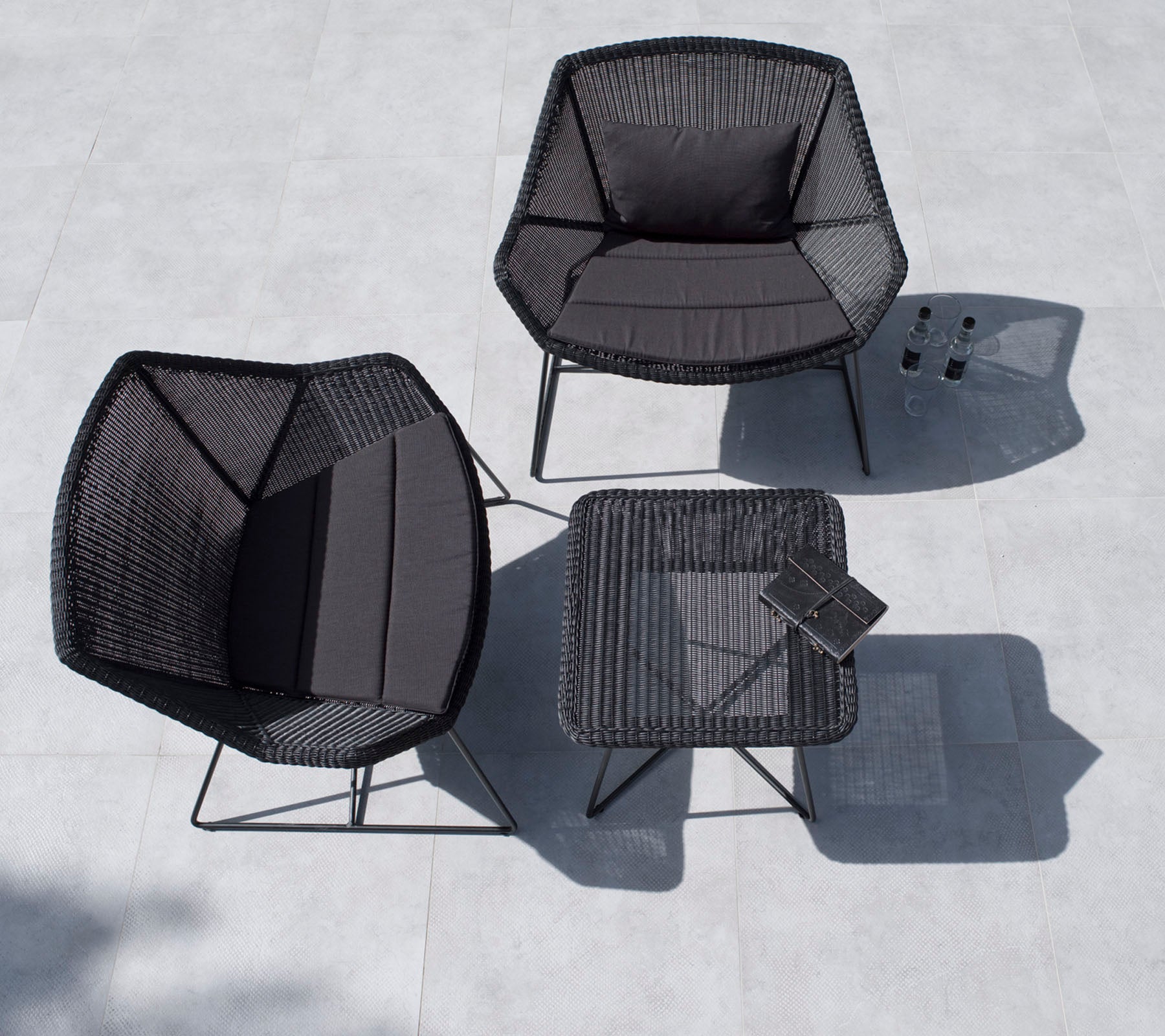 Ensemble de sièges d'extérieur élégant comprenant deux chaises hexagonales et une table carrée, le tout en noir avec un design minimaliste.
