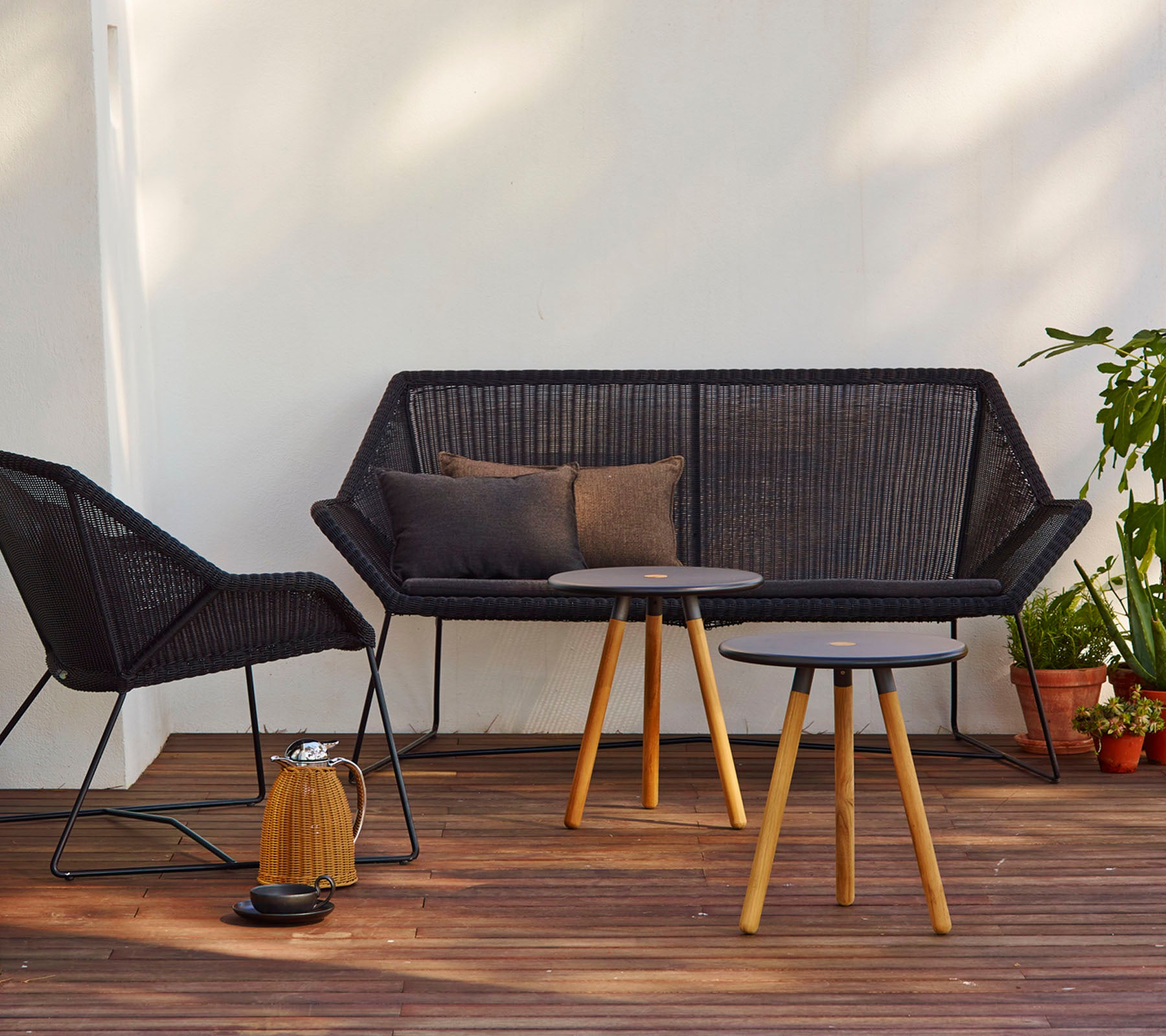 Agencement contemporain avec un canapé noir avec des coussins, une chaise assortie et une table ronde avec des pieds en bois.