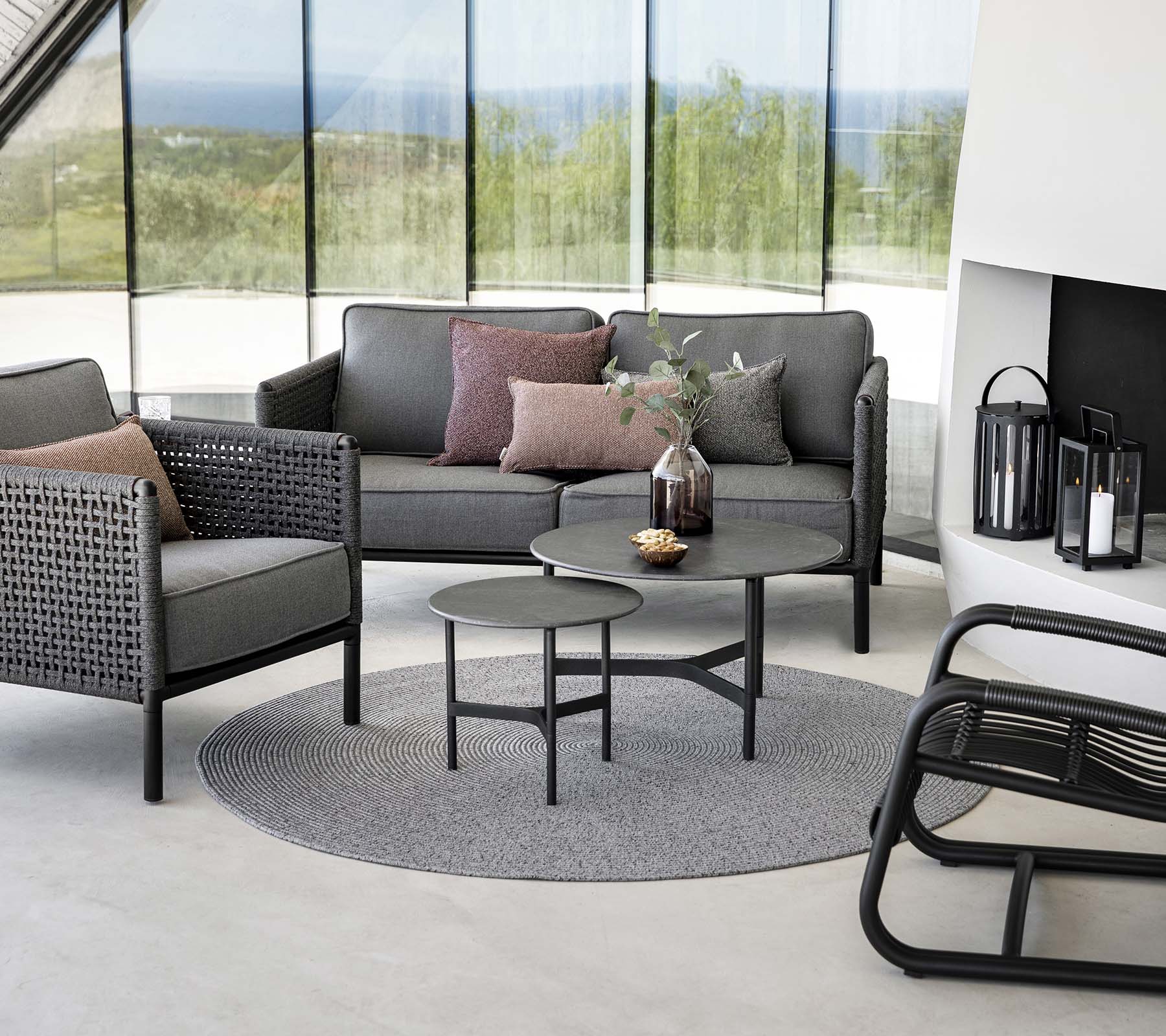 Espace de sièges élégant avec un sofa gris avec des coussins, une table basse ronde et des fauteuils accentués sur un tapis rond. La lumière naturelle améliore l'ambiance.