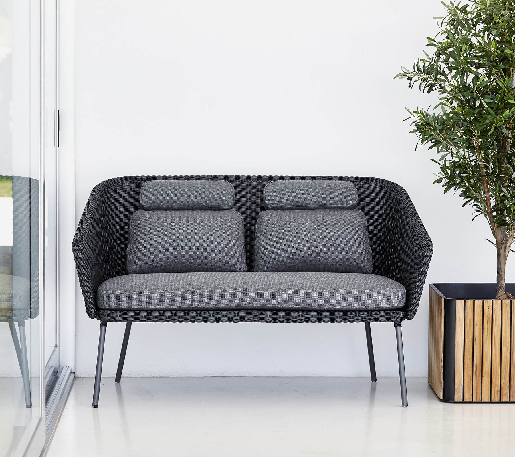 Canapé noir élégant avec des coussins gris, complété par une plante en pot dans un cache-pot en bois. Design moderne et minimaliste.