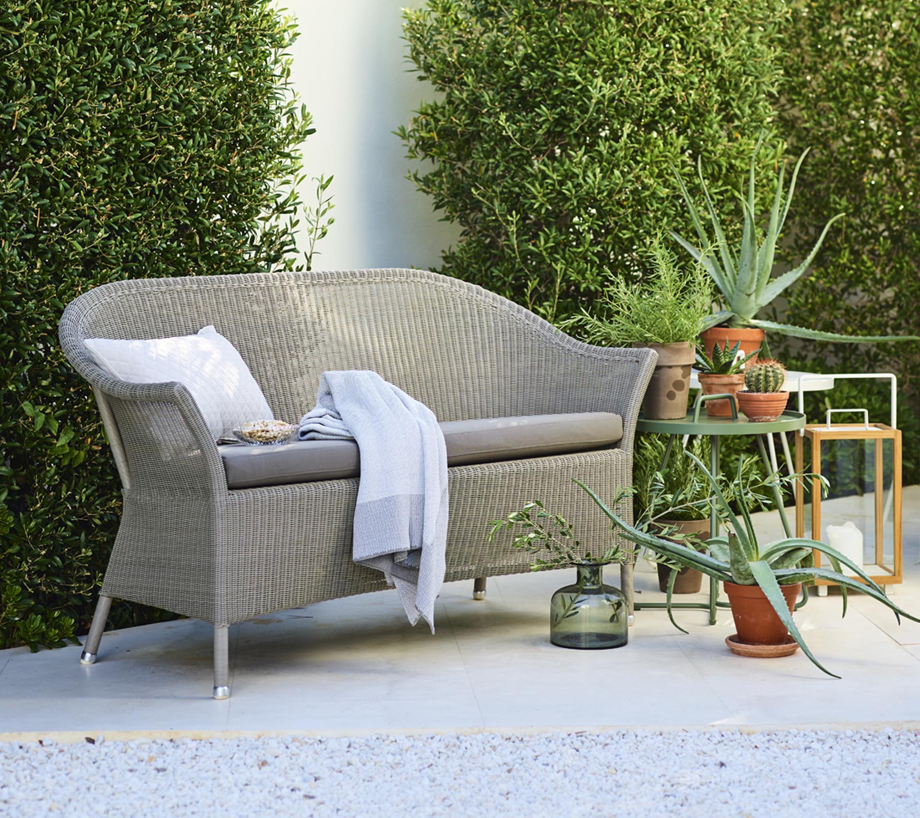 Un loveseat confortable avec des coussins décoratifs, accompagné de plantes en pot et d'une table d'appoint, entouré de verdure.