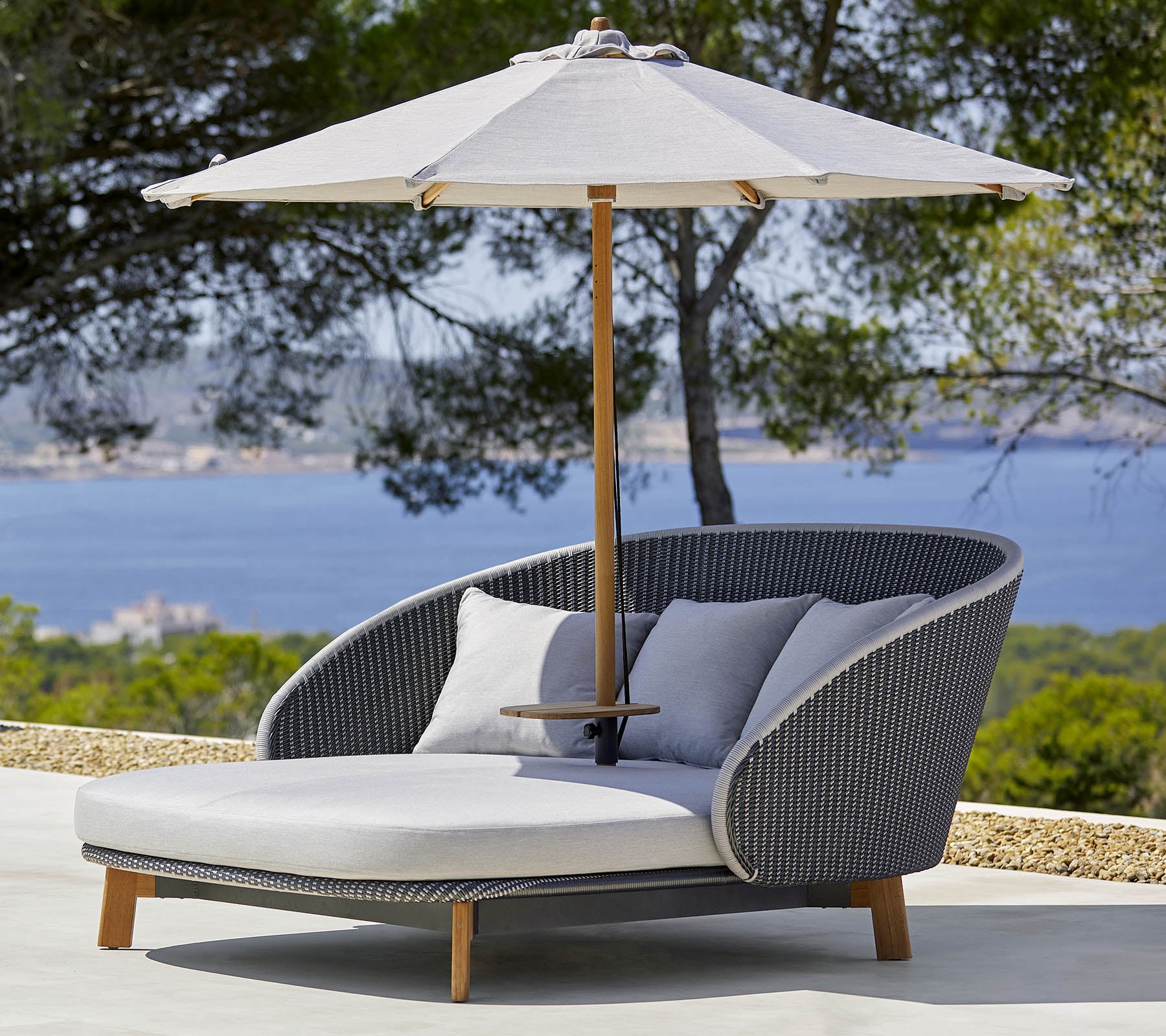 Chaise longue extérieure élégante avec des coussins confortables et un grand parasol pour l'ombre, devant un paysage pittoresque.