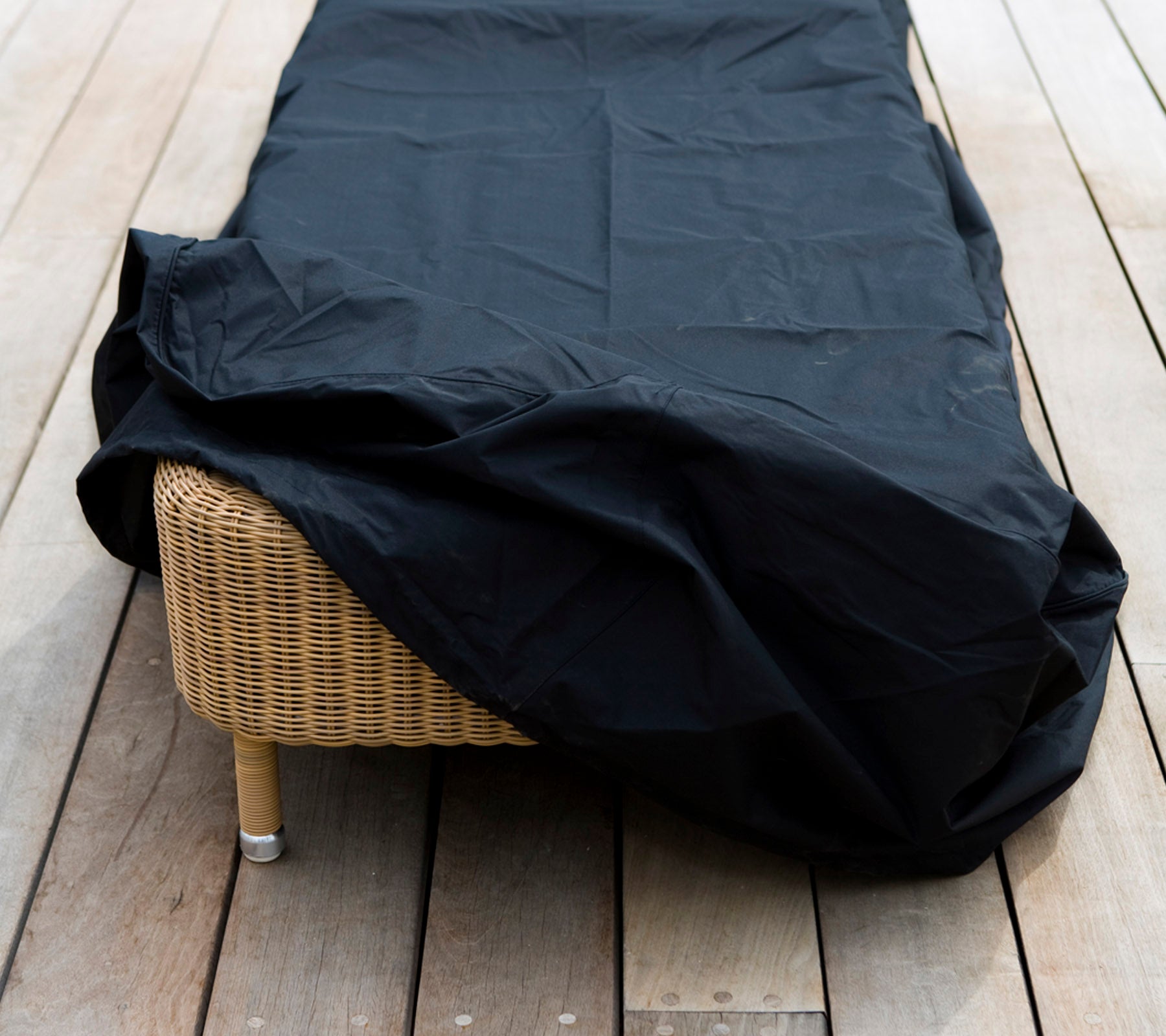 Une pièce de mobilier en osier recouverte d'une housse de protection noire, placée sur une surface en bois.