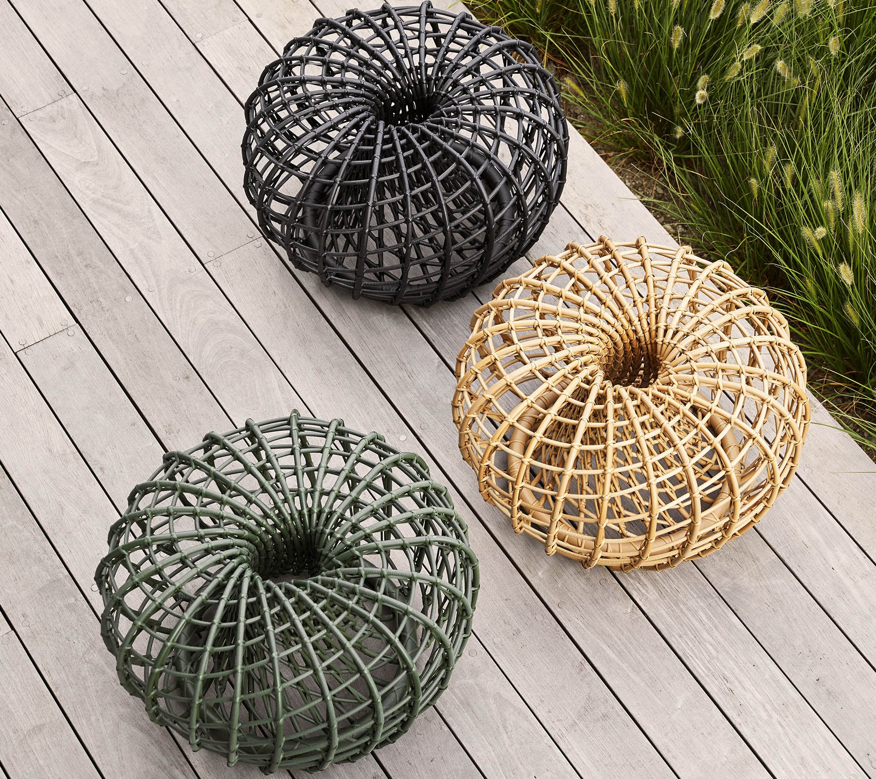 Trois paniers décoratifs tressés en noir, vert et en tons naturels, disposés en un motif circulaire sur une surface en bois.