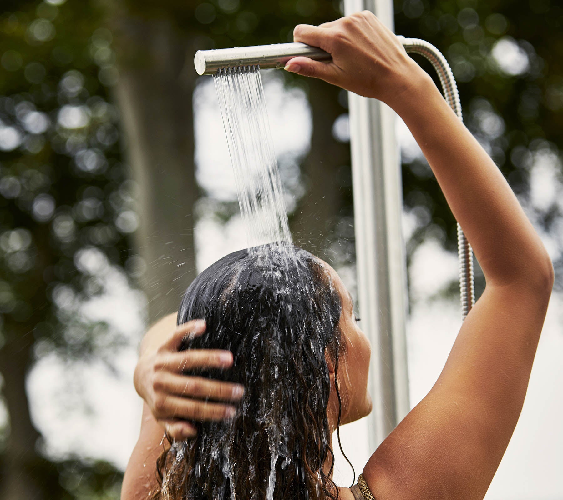 Une personne qui se lave les cheveux sous la douche, avec de l'eau qui cascade et entourée par un cadre naturel.