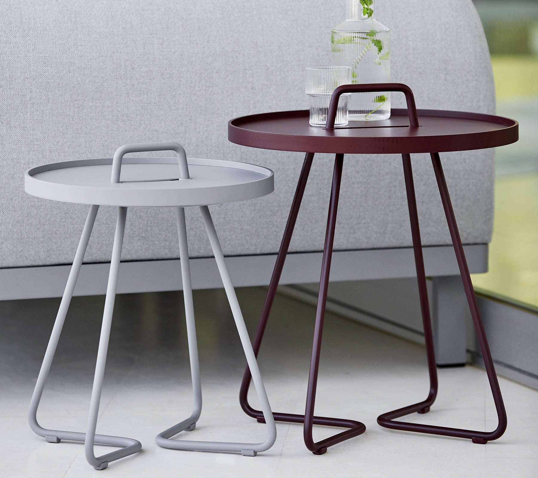 Deux tables d'appoint modernes, une grise et une bordeaux, toutes deux avec des plateaux ronds et des pieds en trépied élégants. Idéal pour une décoration contemporaine.