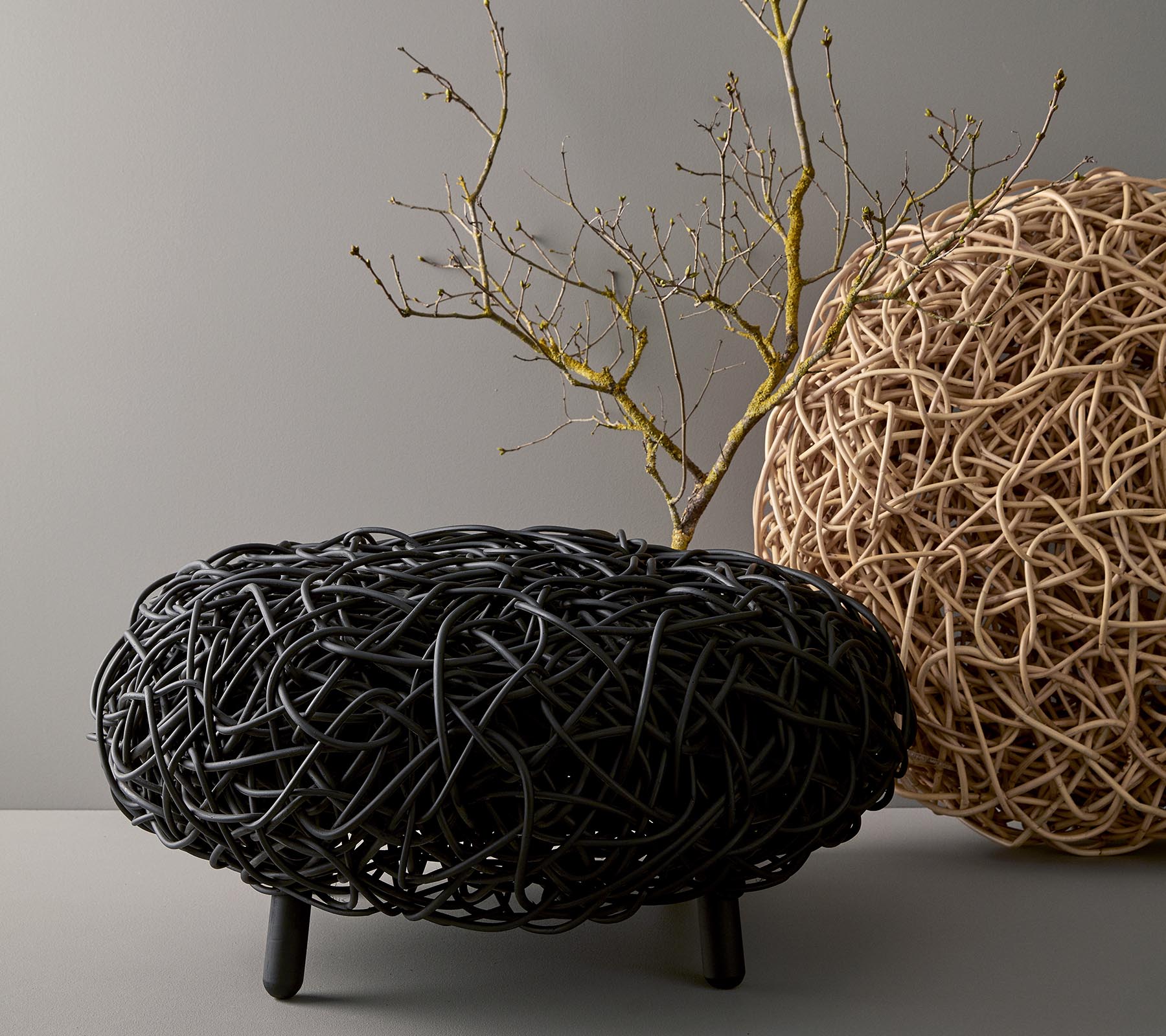 Une table basse ronde et élégante en matériau tressé, présentant des tons noirs et naturels, avec une branche décorative placée sur le dessus.