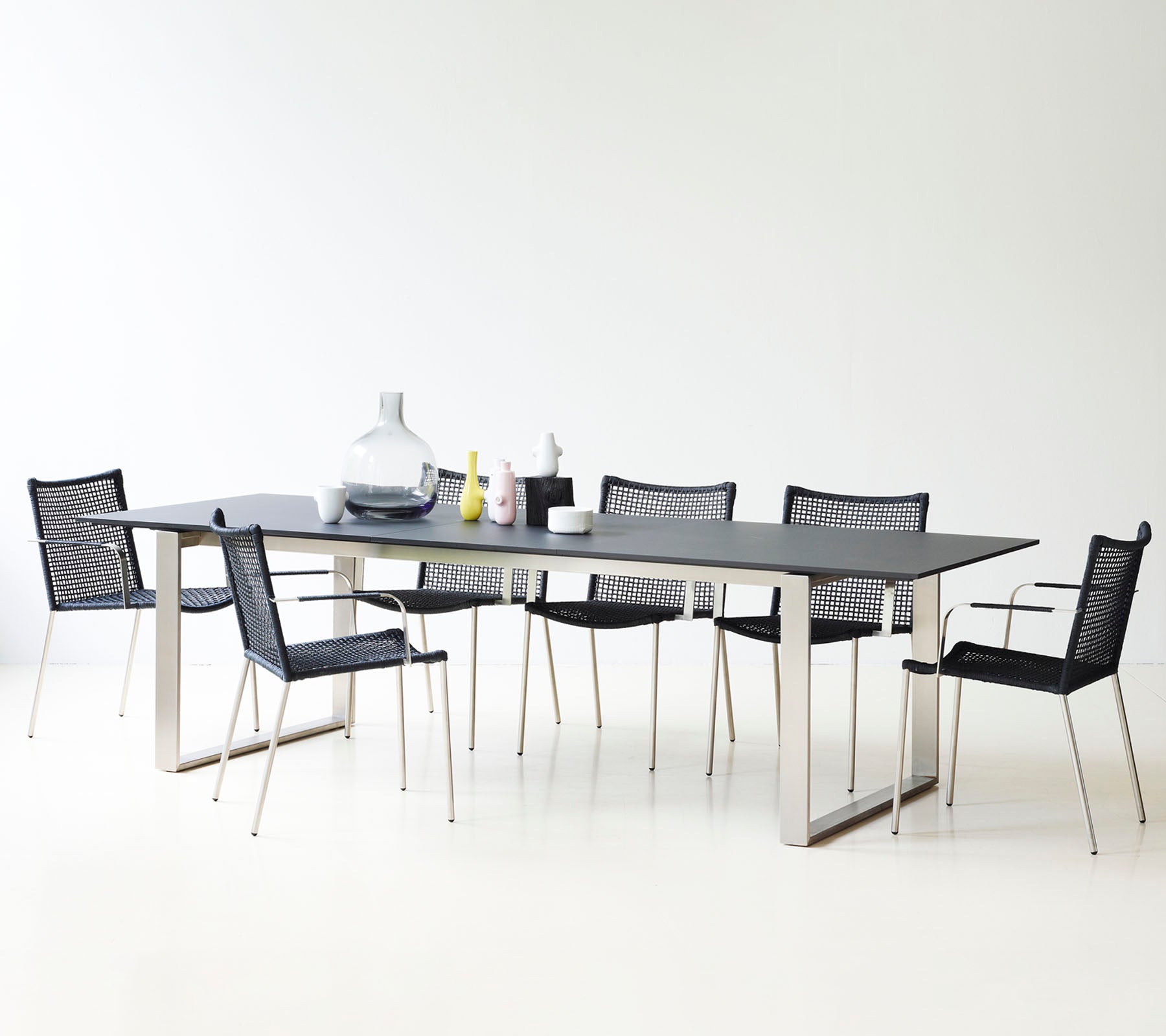 Une table à manger moderne au design épuré, entourée de chaises en mesh noires élégantes et de vases décoratifs.