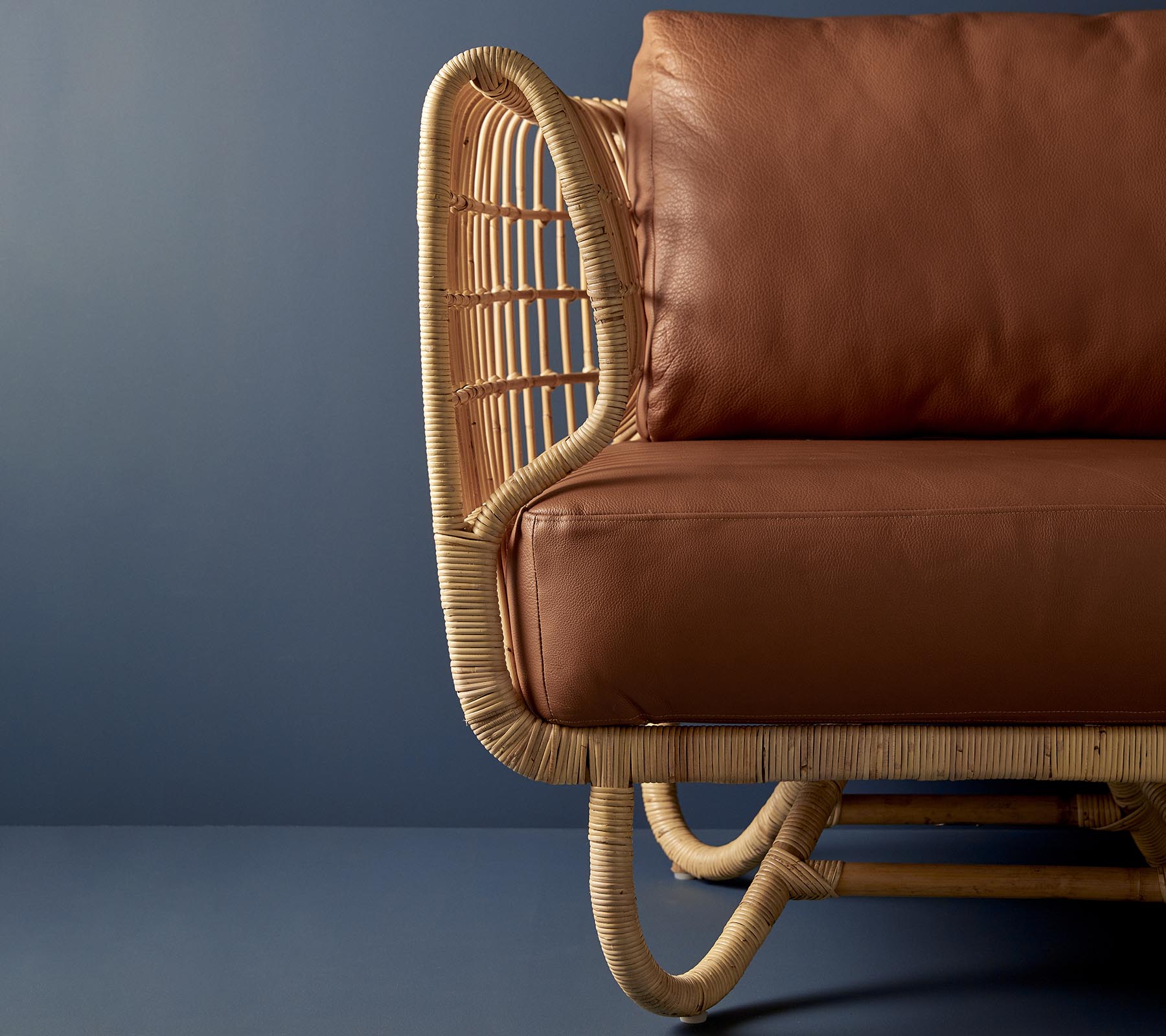 Chaise en rotin au design courbé et coussins en cuir marron, mettant en valeur un mélange de matériaux naturels et d'esthétique moderne.