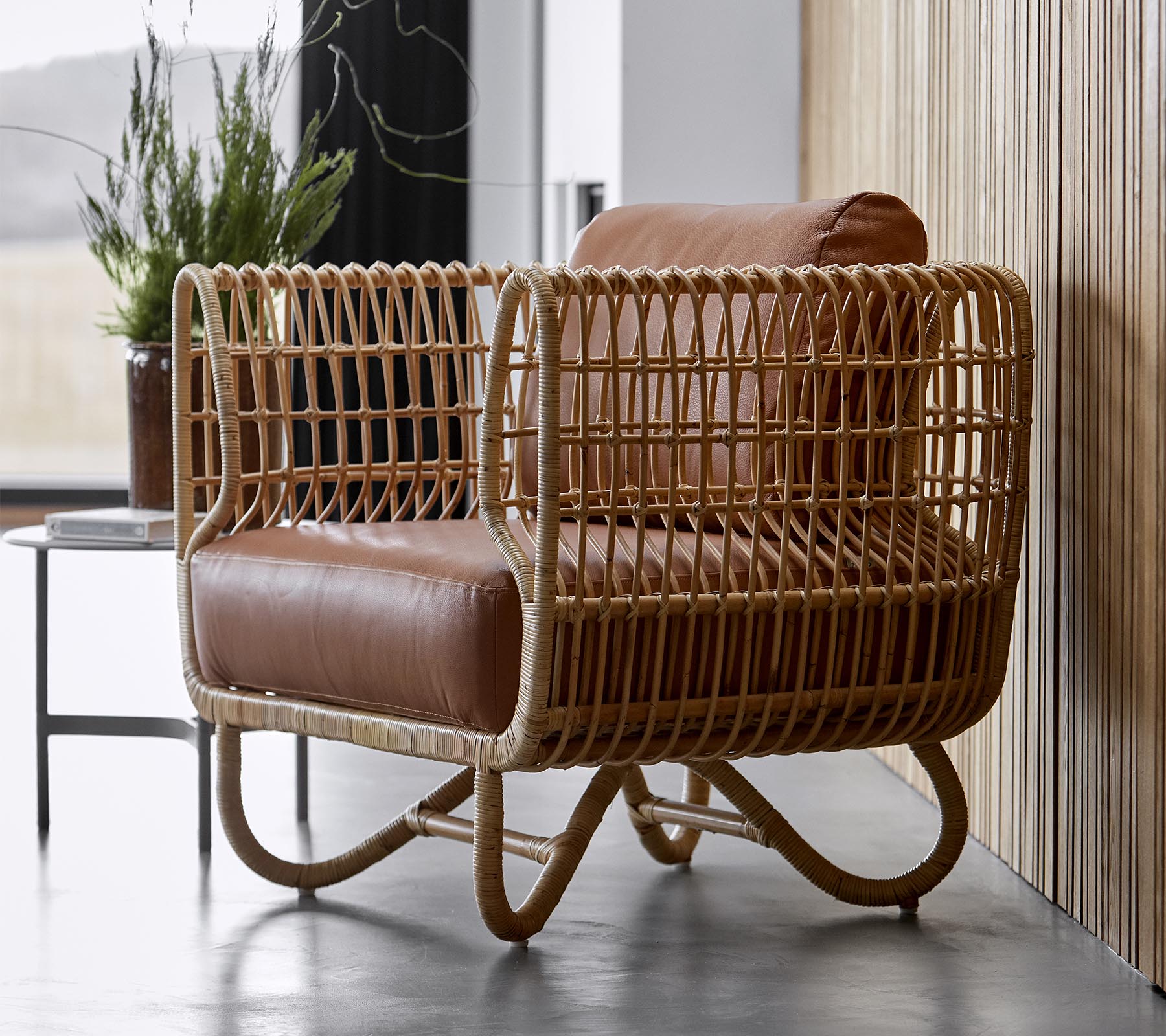 Fauteuil élégant avec un cadre en rotin tissé et des coussins en cuir brun moelleux, parfait pour une décoration moderne.