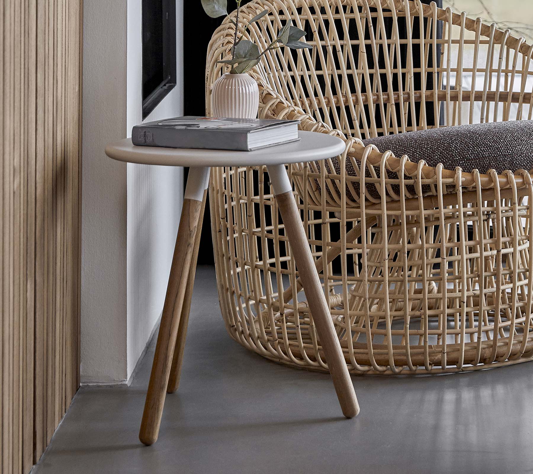 Une table d'appoint ronde avec une surface claire et des pieds en bois, positionnée à côté d'une chaise tissée.
