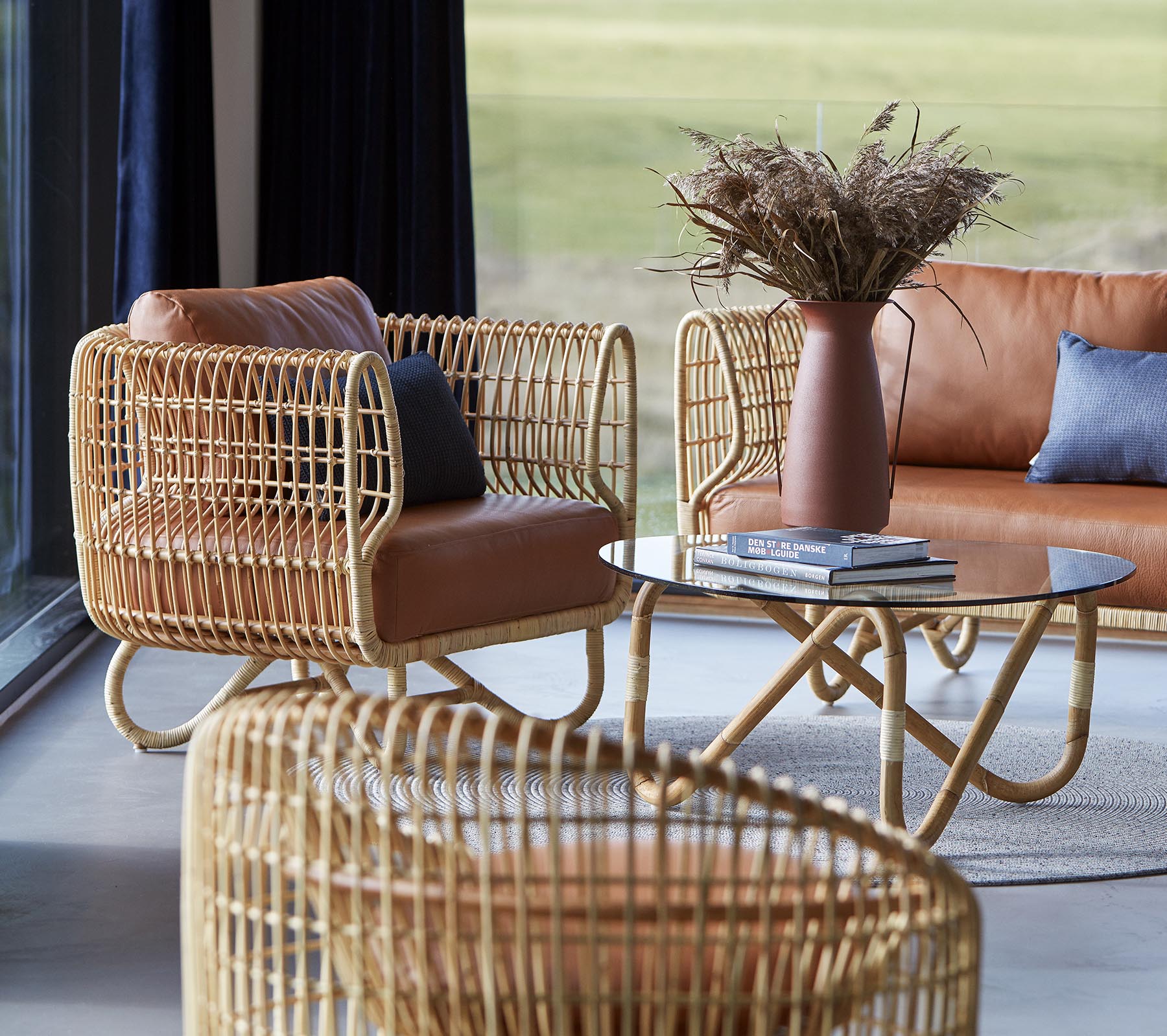 Des sièges élégants avec des cadres en rotin tressé, des coussins en cuir, une table basse épurée et un vase avec du feuillage séché, créant une atmosphère chaleureuse.