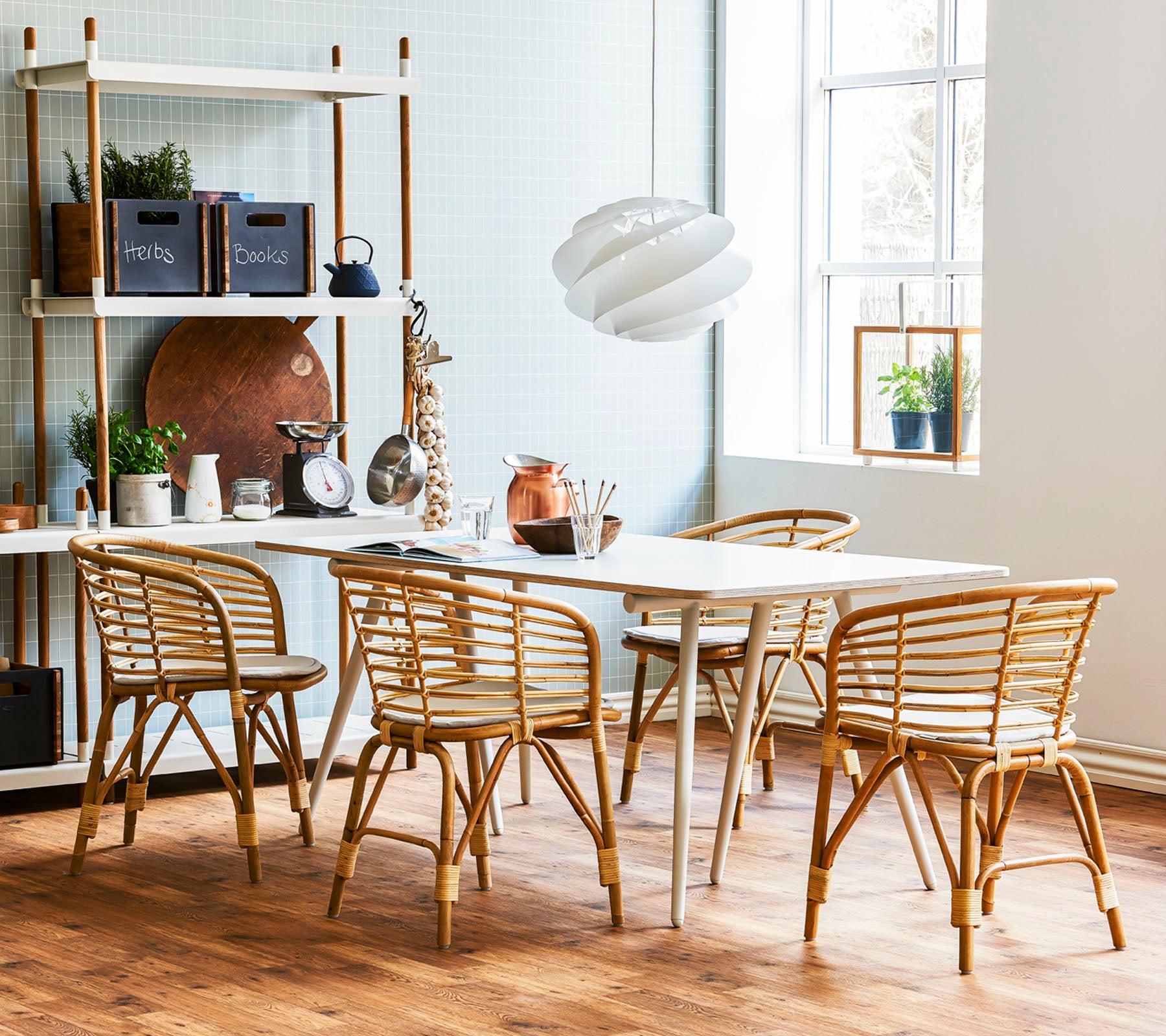 Une salle à manger élégante avec une table en bois clair entourée de chaises en rotin et d'une suspension moderne, complétée par des étagères décoratives.