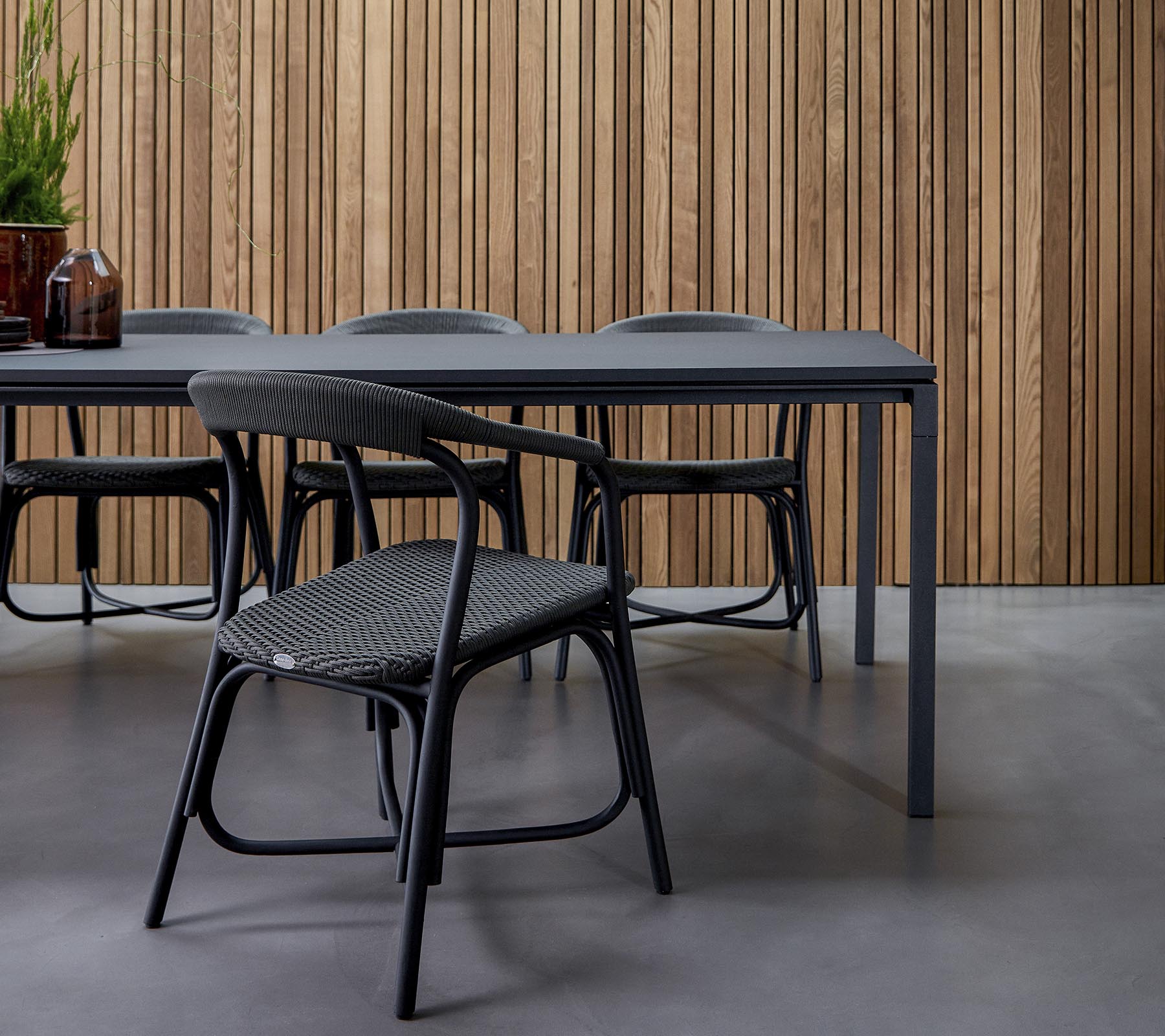 Une salle à manger moderne avec une table élégante entourée de chaises stylées, contre un fond en bois texturé.