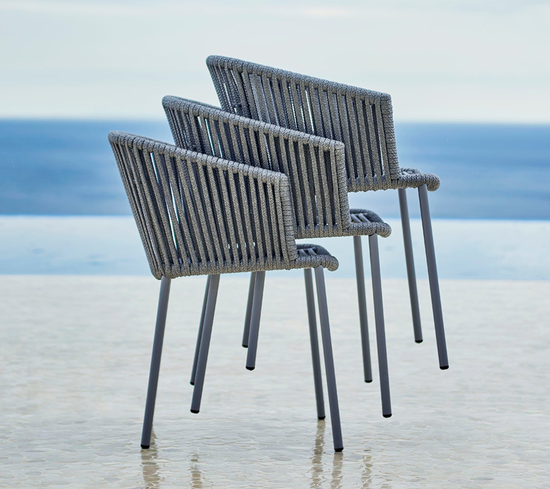Trois chaises modernes au design élégant, avec un dossier à lattes et des accoudoirs, positionnées à côté d'une vue apaisante sur l'eau.