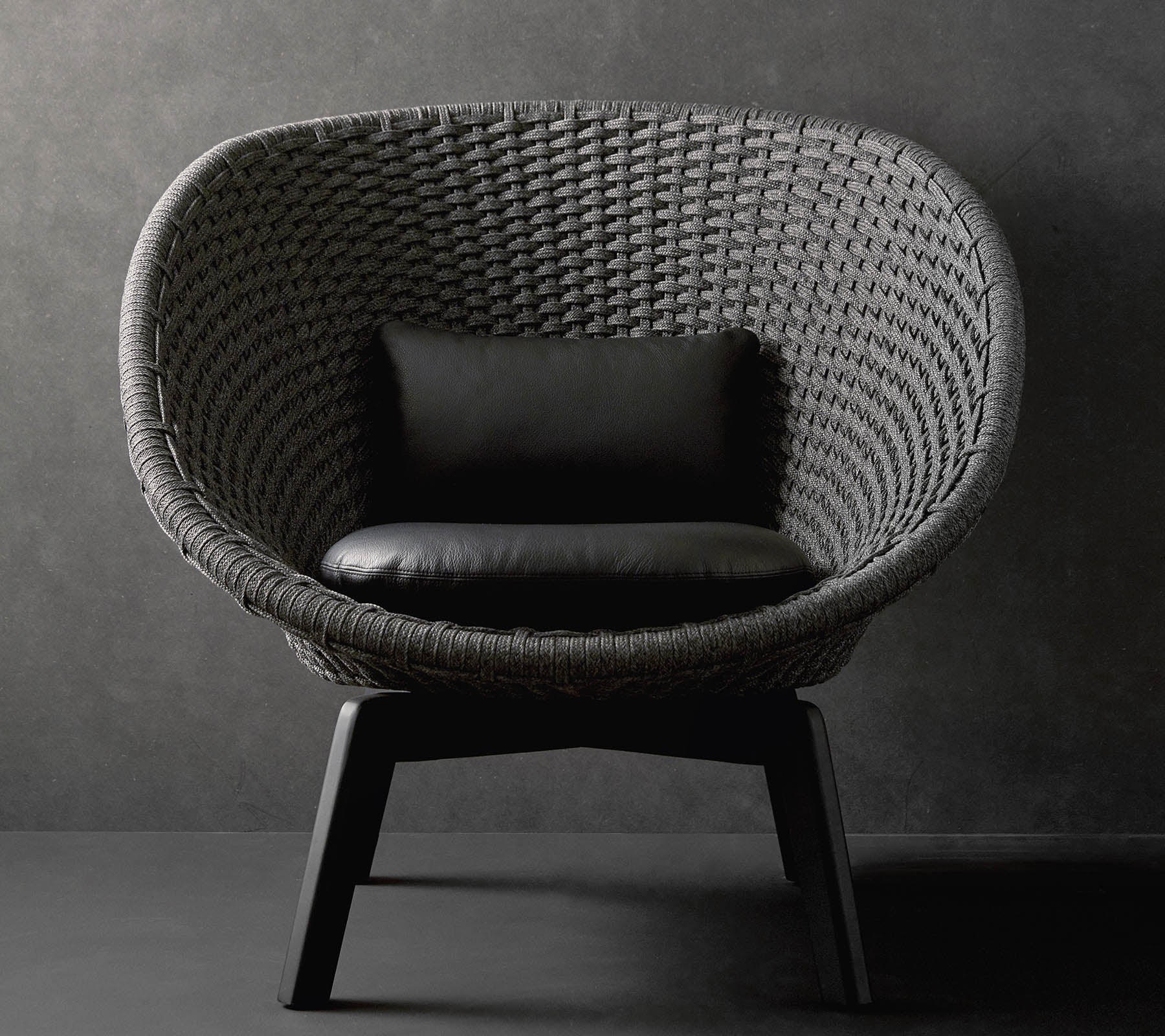 Une chaise ronde élégante avec un design tissé texturé et un coussin noir, reposant sur des pieds en bois élégants contre un fond sombre.
