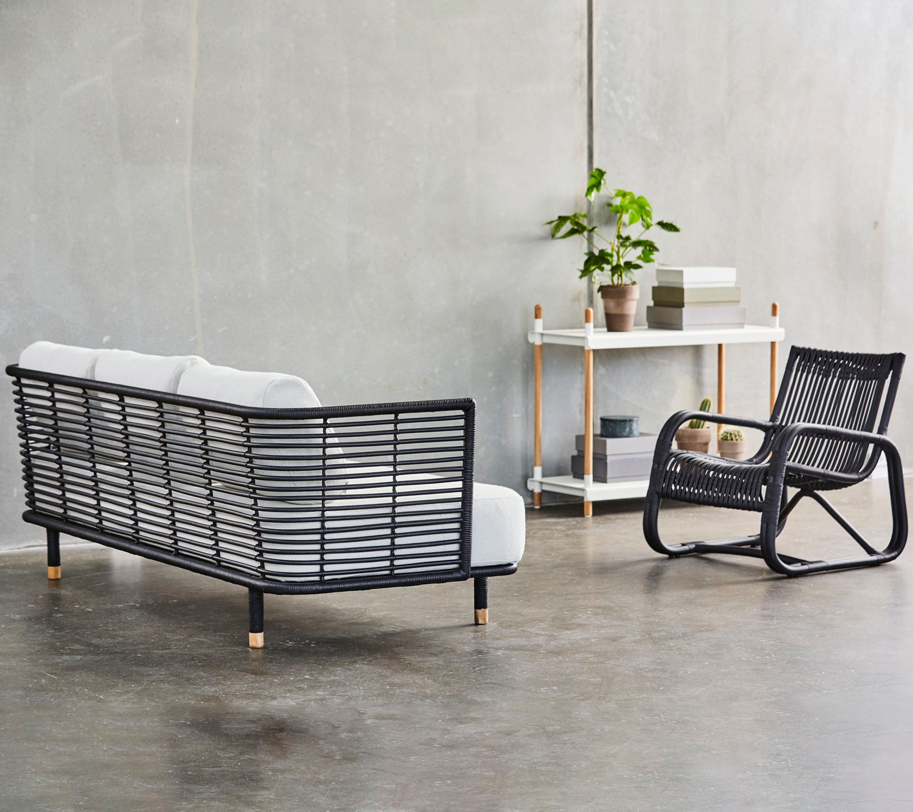 Un aménagement moderne avec un canapé à cadre noir élégant, des coussins blancs et un rocking chair assorti, accompagné de verdure.