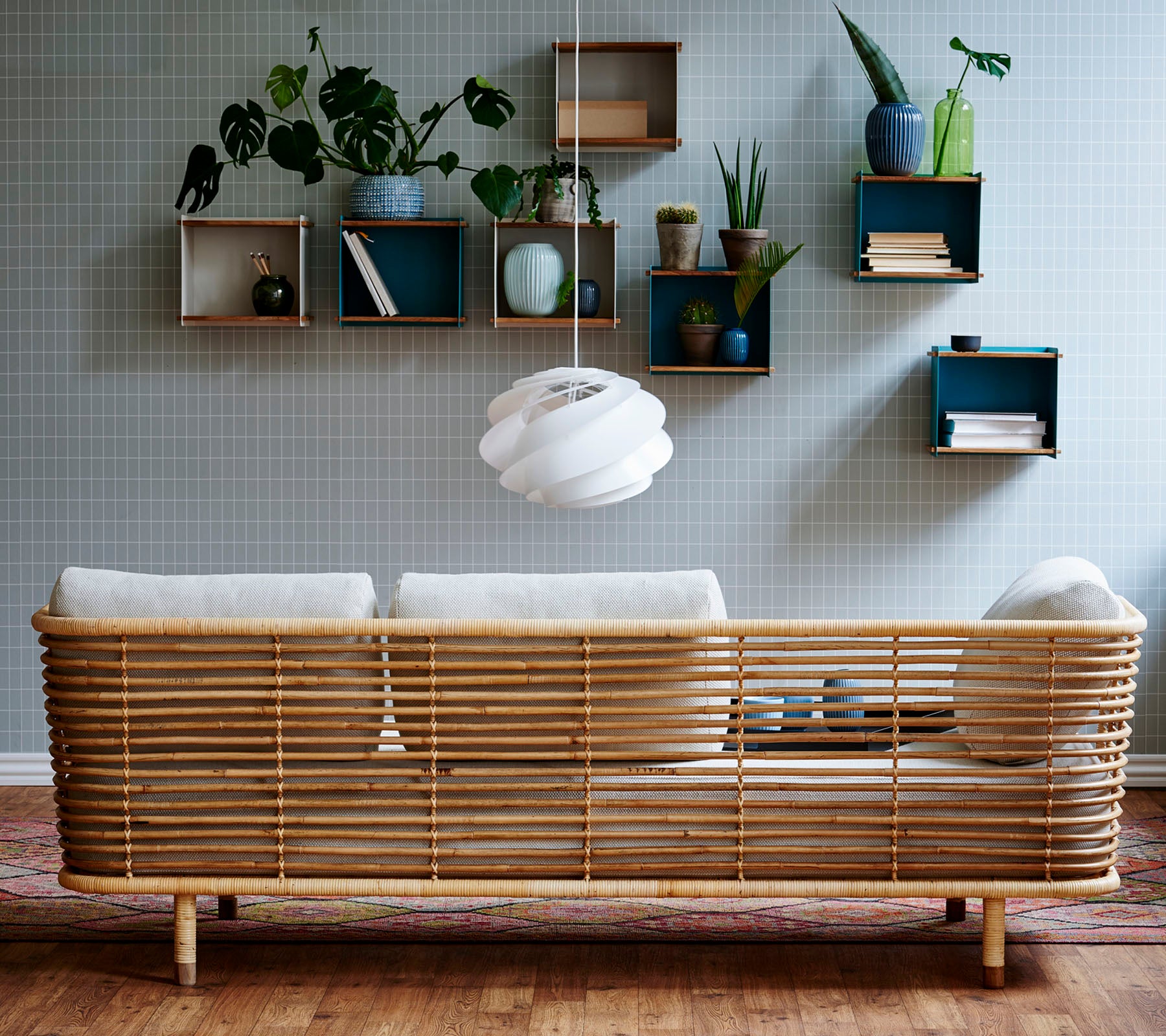 Un canapé en rotin élégant avec des coussins clairs contre un mur texturé, complété par des étagères murales affichant des plantes et des objets décoratifs.