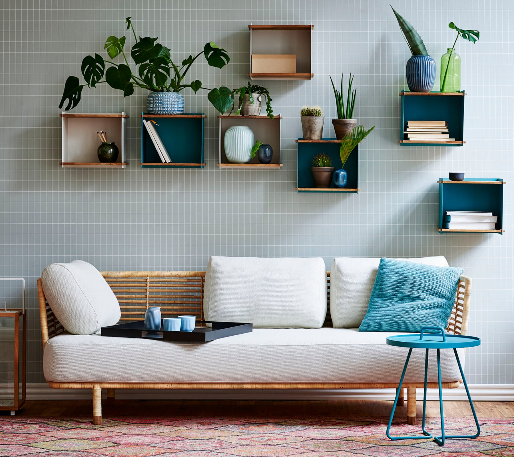 Un canapé élégant avec un coussin léger et une petite table, orné de diverses plantes en pot présentées sur des étagères géométriques.