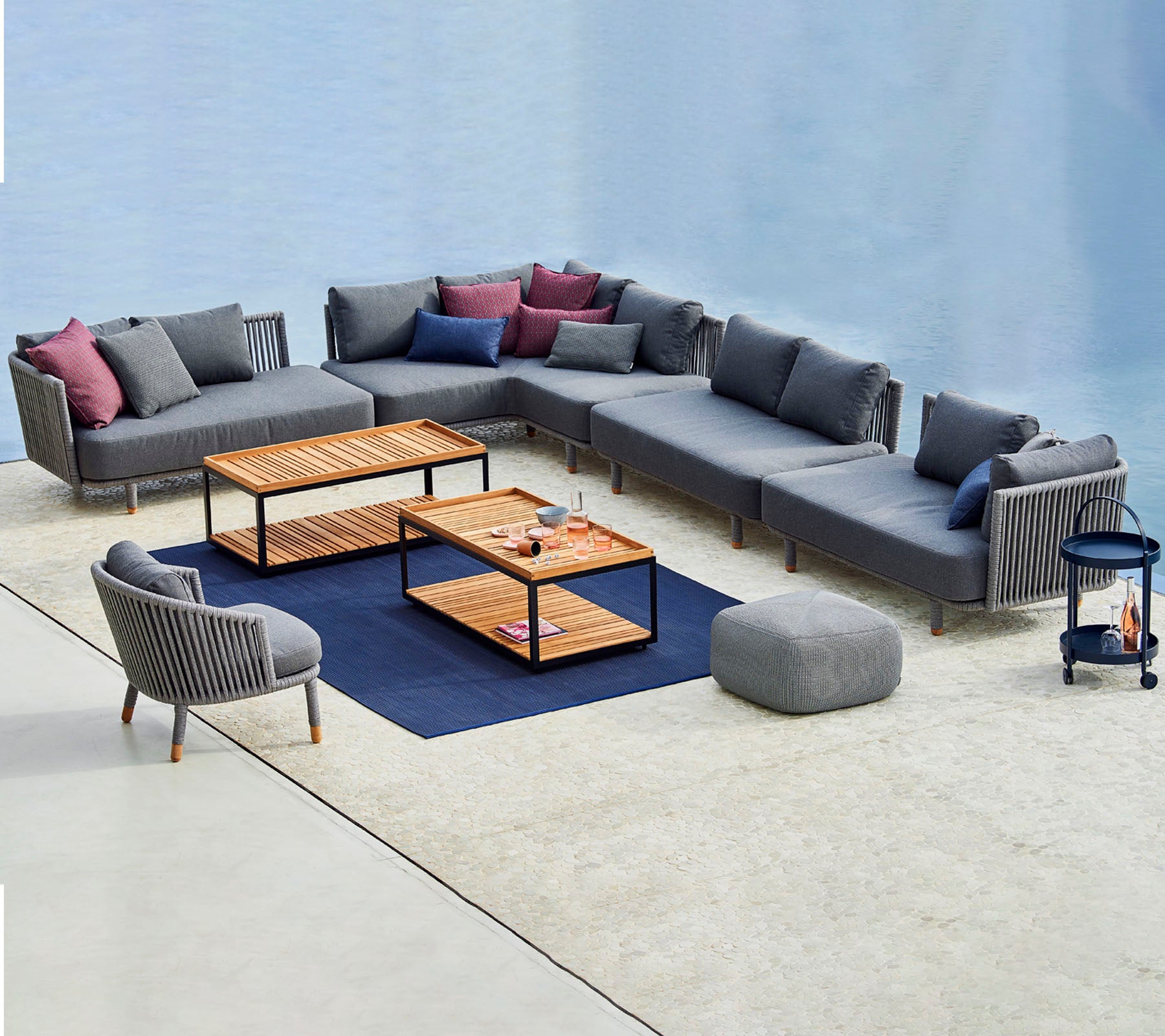 Agencement contemporain de sièges avec un canapé modulaire gris, des coussins colorés, des tables basses et une chaise d'appoint assortie.